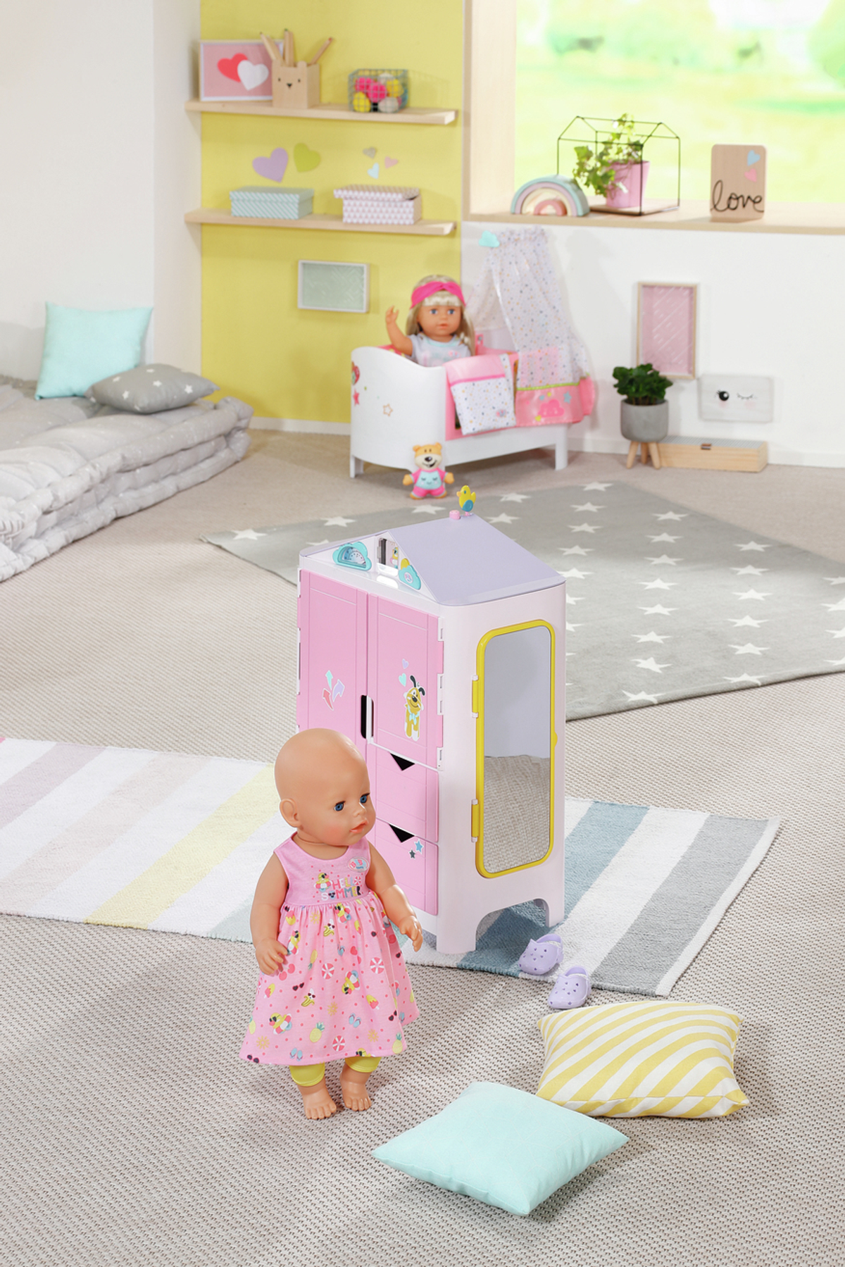 Eine Puppe mit rosa Kleid steht vor einem rosa Puppenhaus mit Zubehör und anderen Spielzeugen.