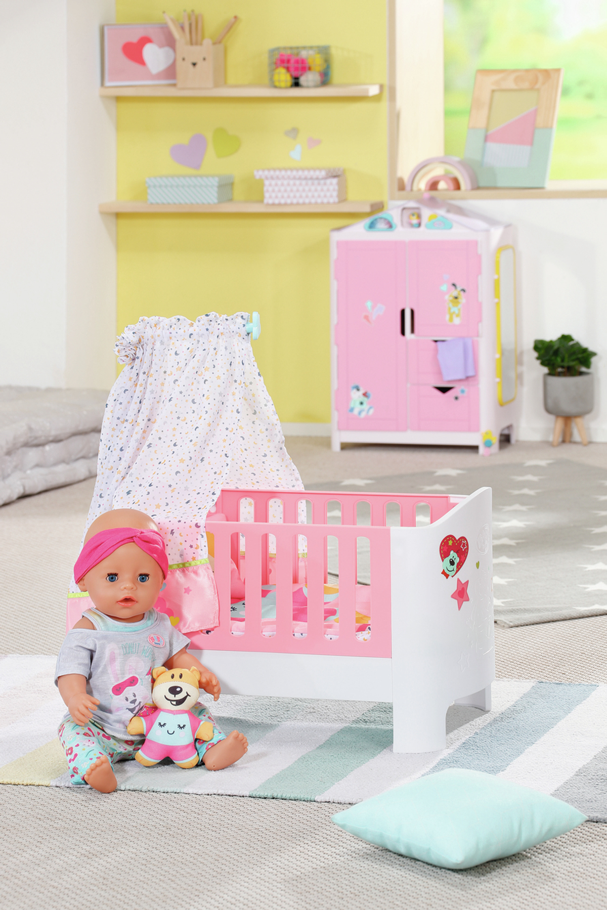 Babypuppe in einem Kinderbett neben einem Kleiderschrank. Hellgrün und rosa. Heller Hintergrund.