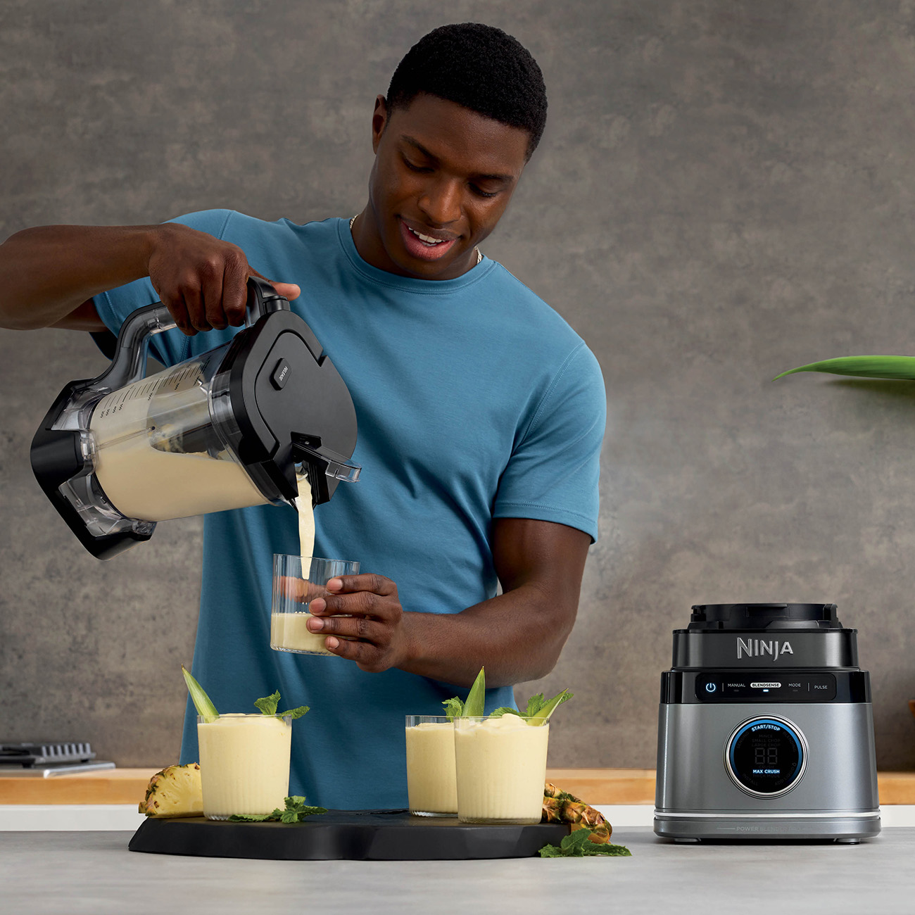 Mężczyzna nalewa smoothie do szklanki. Blender i przygotowane napoje na stole.