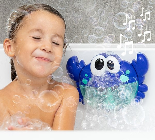 Ein Mädchen in der Badewanne mit Blasen, lächelt einen Blasen blasenden Krabben-Spielzeug an.