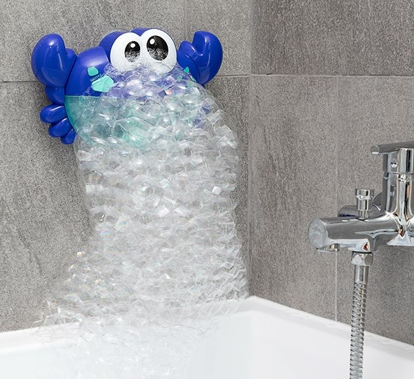 Eine blaue Krabben-Blasenmaschine ist an einer grauen Wand über einer Badewanne befestigt. Blasen strömen aus ihr.