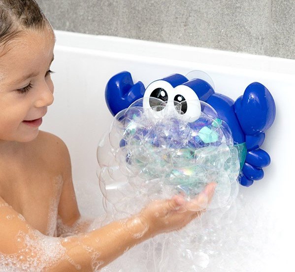 Junges Mädchen spielt mit einem blauen Krebs-Blasenspielzeug in einer mit Blasen gefüllten Badewanne.