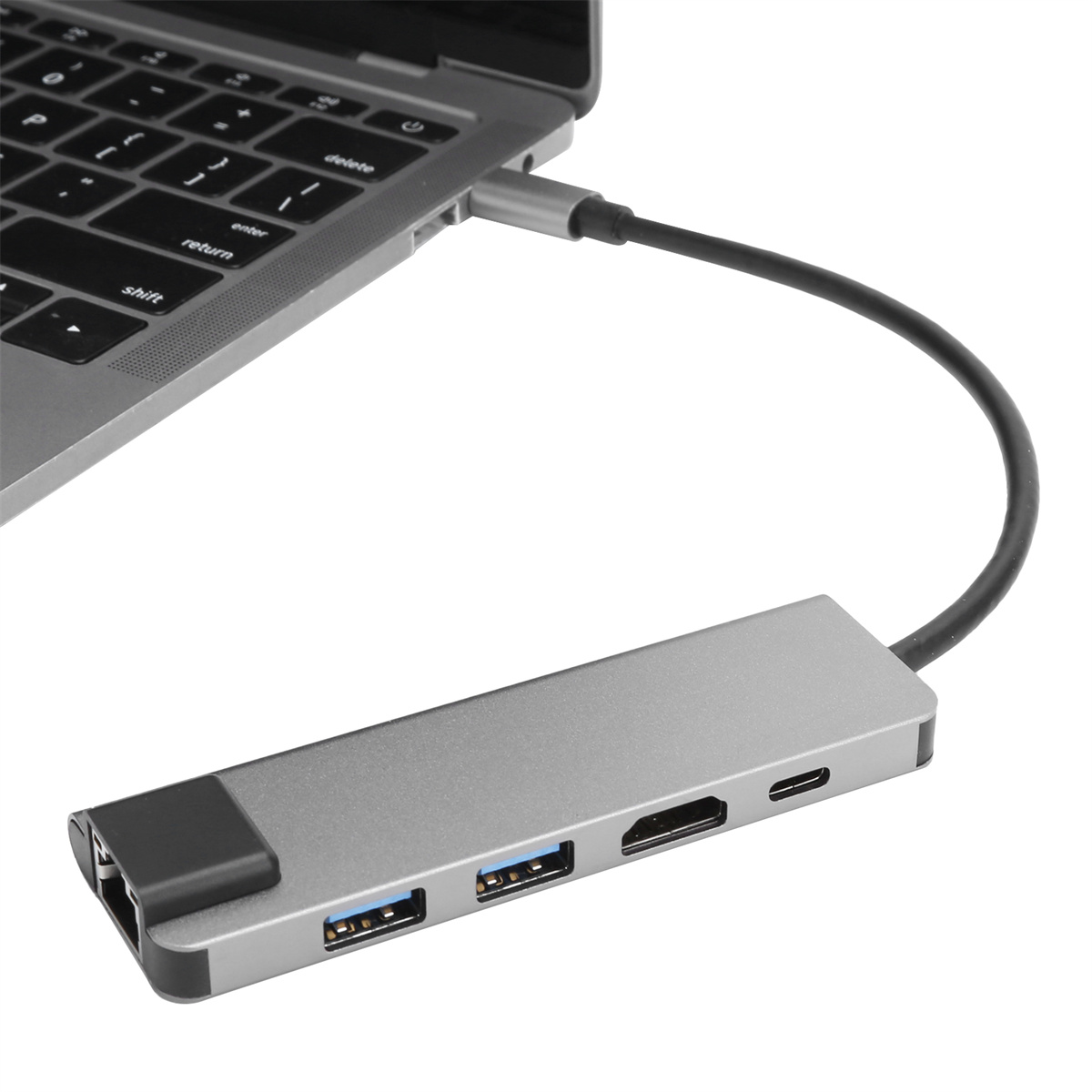 Ein Laptop, der mit einem silbernen Hub mit USB-Anschlüssen, HDMI und anderen Anschlüssen verbunden ist.