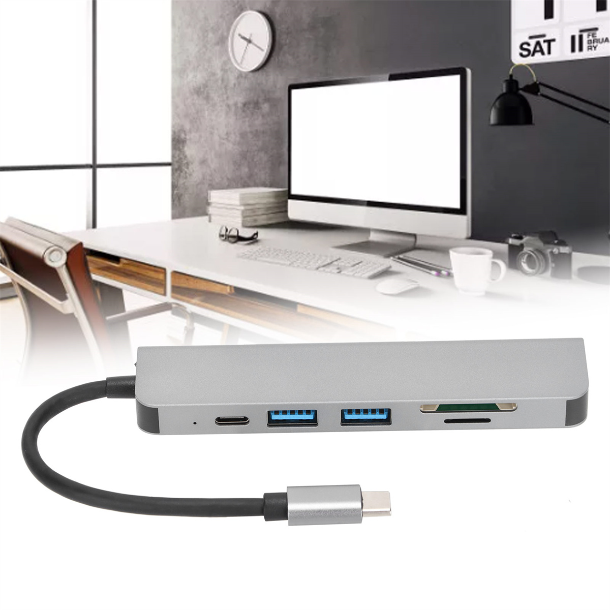 Silberner USB-Hub mit mehreren Anschlüssen und einem schwarzen Kabel auf einem Schreibtisch.