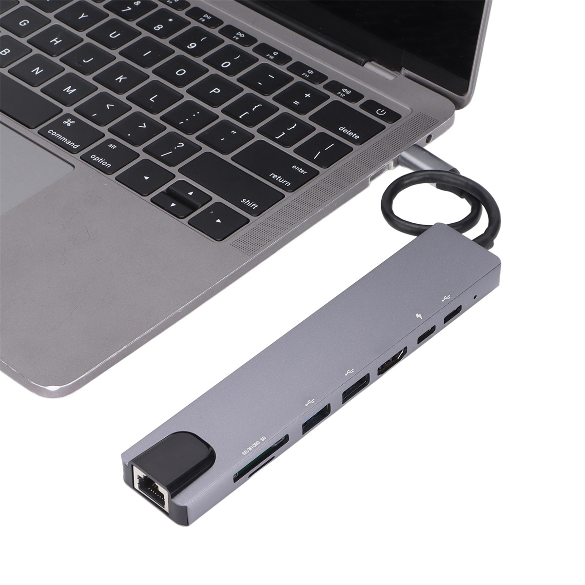 Das Bild zeigt einen grauen USB-C-Hub, der mit einem Laptop verbunden ist und mehrere Anschlüsse wie USB und SD-Kartenleser aufweist.