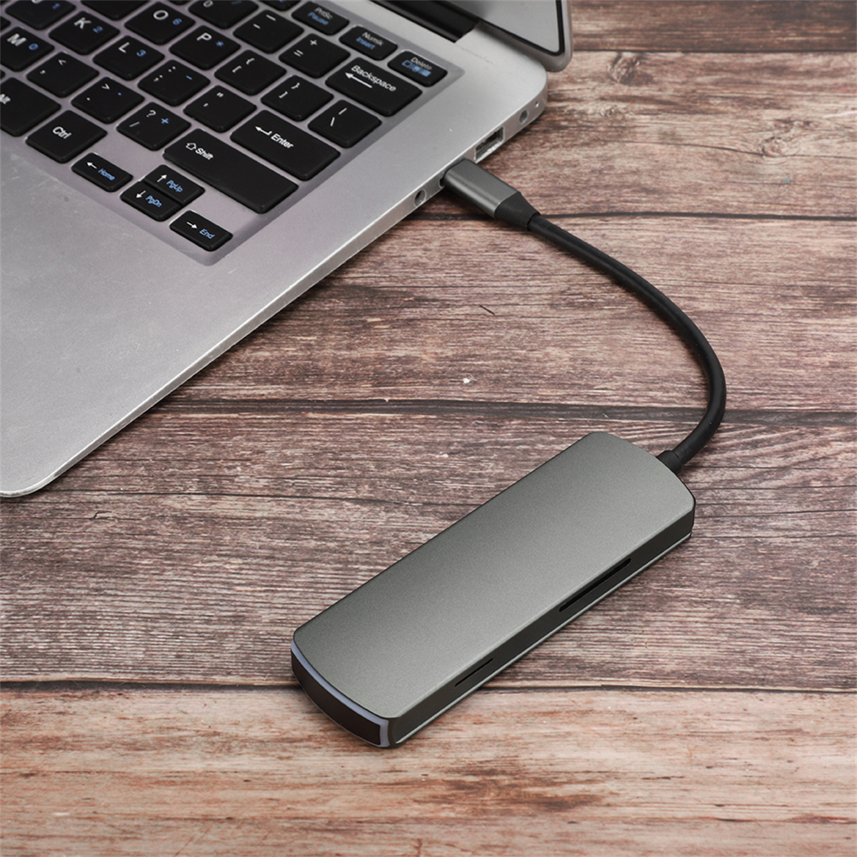 Laptop mit einem grauen USB-Hub verbunden. Der Hub befindet sich auf einem Holztisch.