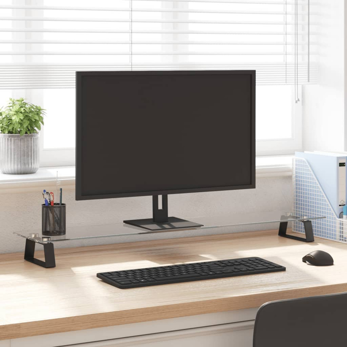 Ein Schreibtisch mit Monitor, Tastatur und einer grünen Pflanze am Fenster.