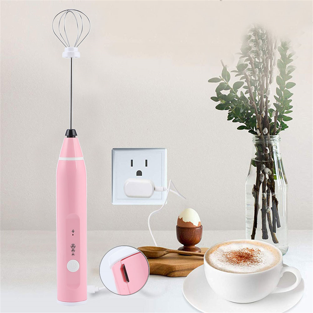 Rosa Handmixer, der geladen wird, neben Kaffee, Ei und Vase.