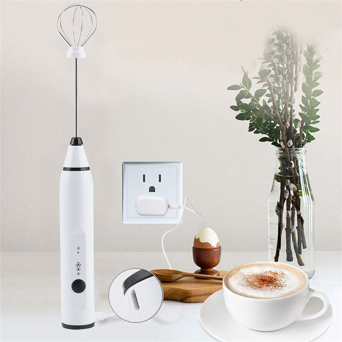 Ein weißer elektrischer Schneebesen und ein Ladekabel, das an eine Steckdose angeschlossen ist. Enthält eine Kaffeetasse.