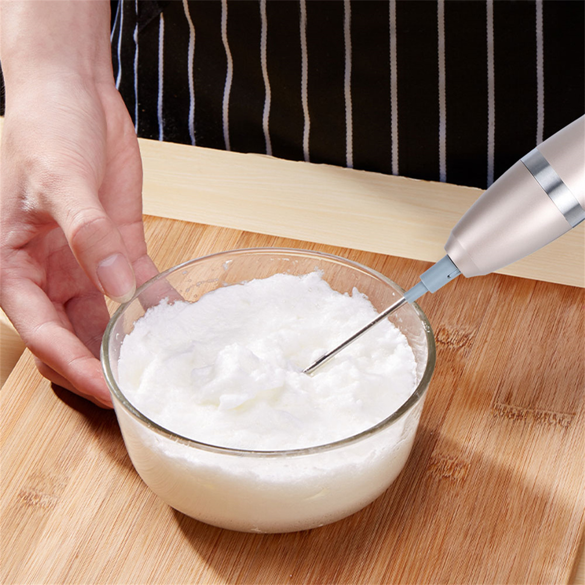Hand hält Mixer über einer Glasschüssel mit Schlagsahne.