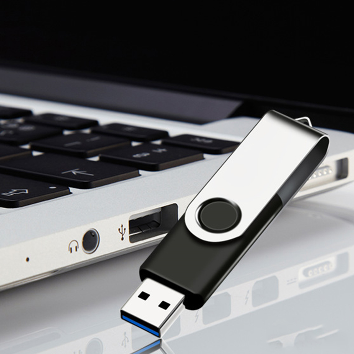 Ein schwarzer und silberner USB-Stick, der an einen Laptop angeschlossen ist. Der Laptop ist geöffnet.