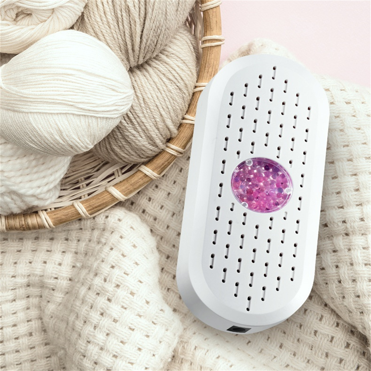 Weißer Luftentfeuchter mit lila Perlen, in der Nähe eines Garnkorbs und einer Strickdecke.