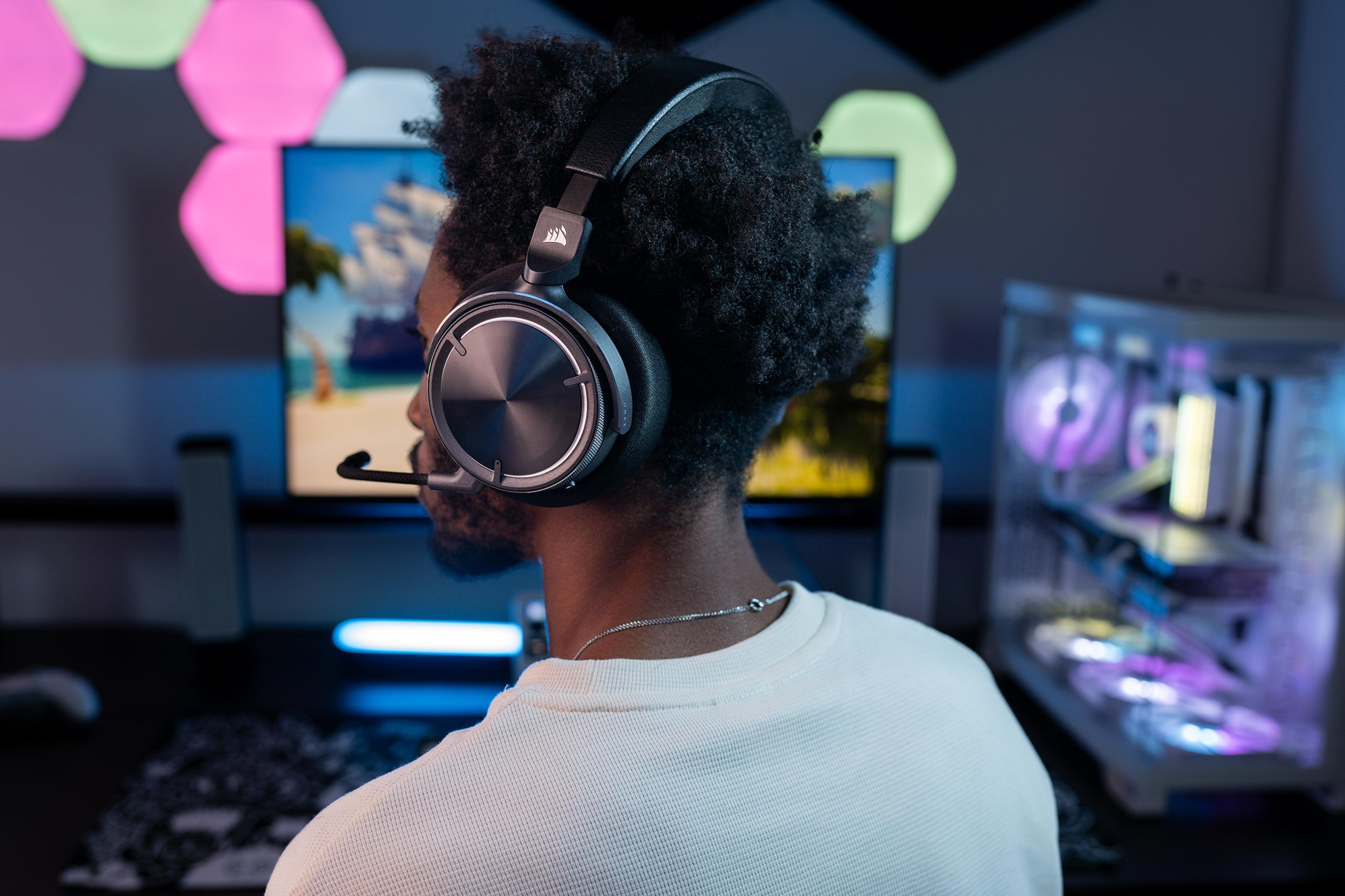 Un uomo con le cuffie, guarda uno schermo del computer. È visibile una configurazione di gioco con luci colorate.
