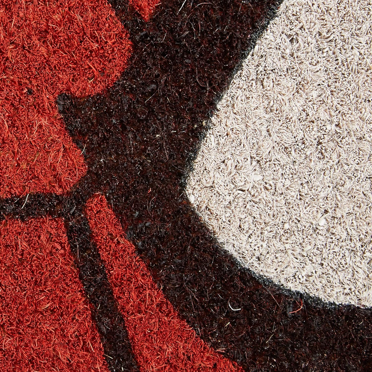 Primer plano de una alfombra con diseño rojo y blanco. Textura áspera con detalles marrón oscuro y blanco.