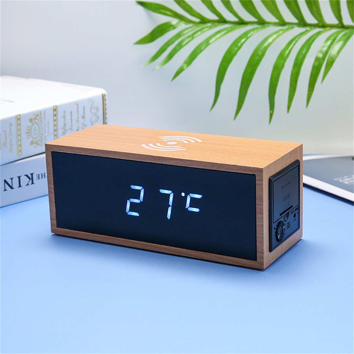 Eine Holzuhr mit blauem Display, das 27°C anzeigt, mit einem drahtlosen Ladesymbol.