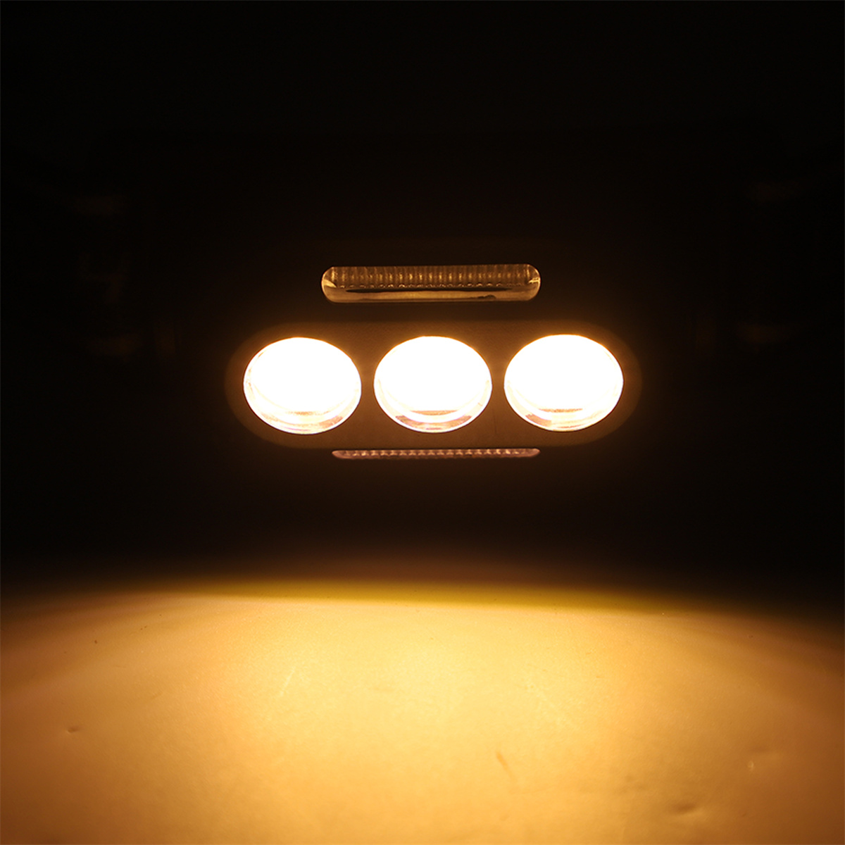 Drei helle Lichter in einer horizontalen Reihe vor dunklem Hintergrund, mit gelbem Schimmer.
