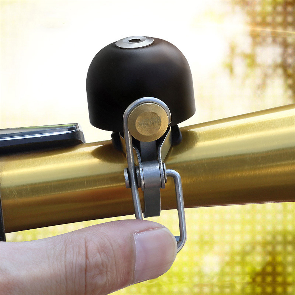 Eine schwarze Fahrradklingel, die an einem goldenen Lenker montiert ist, mit einem Finger, der auf die Klingel drückt.