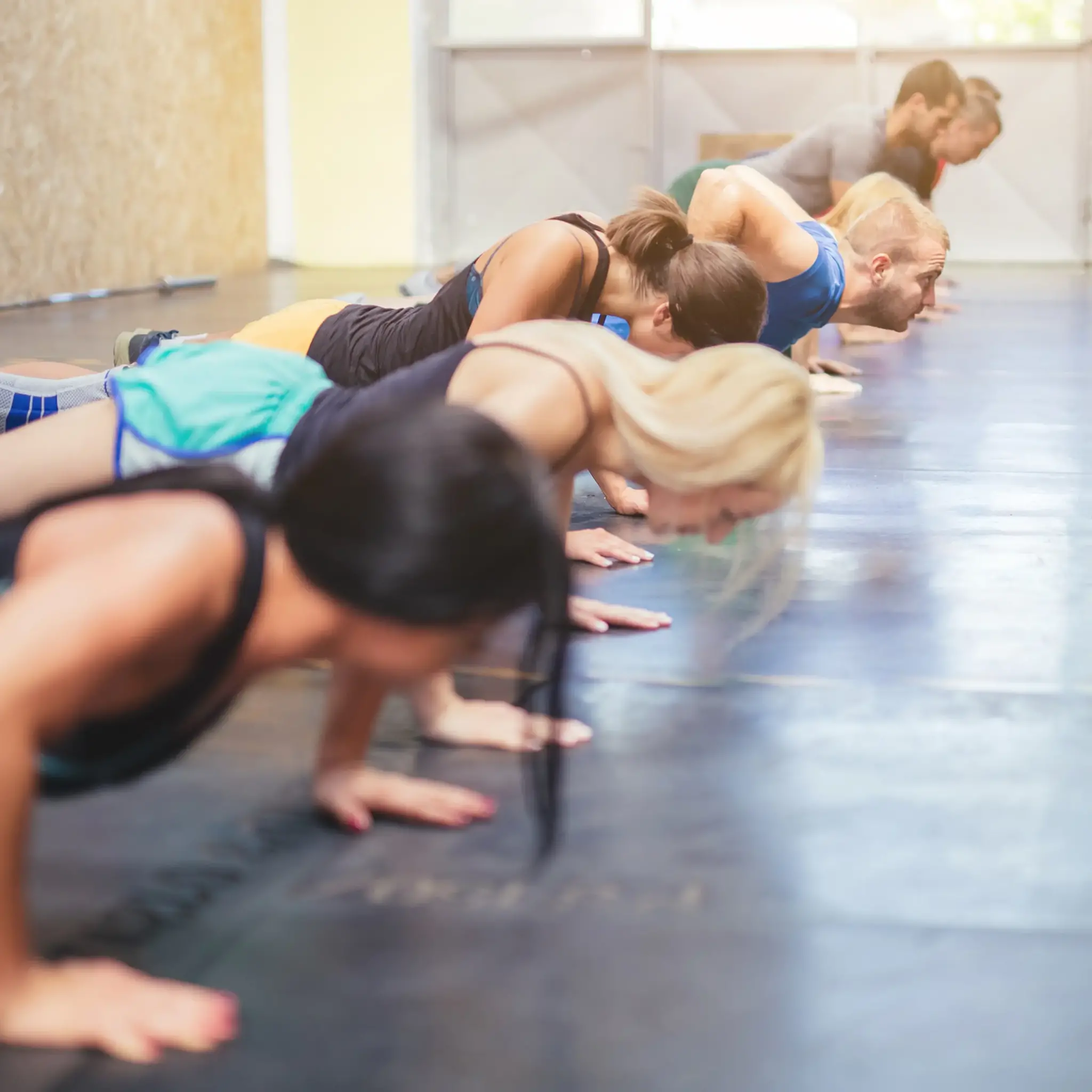 Leute machen Liegestütze auf einem Fitnessstudioboden. Sie trainieren in einer Reihe.