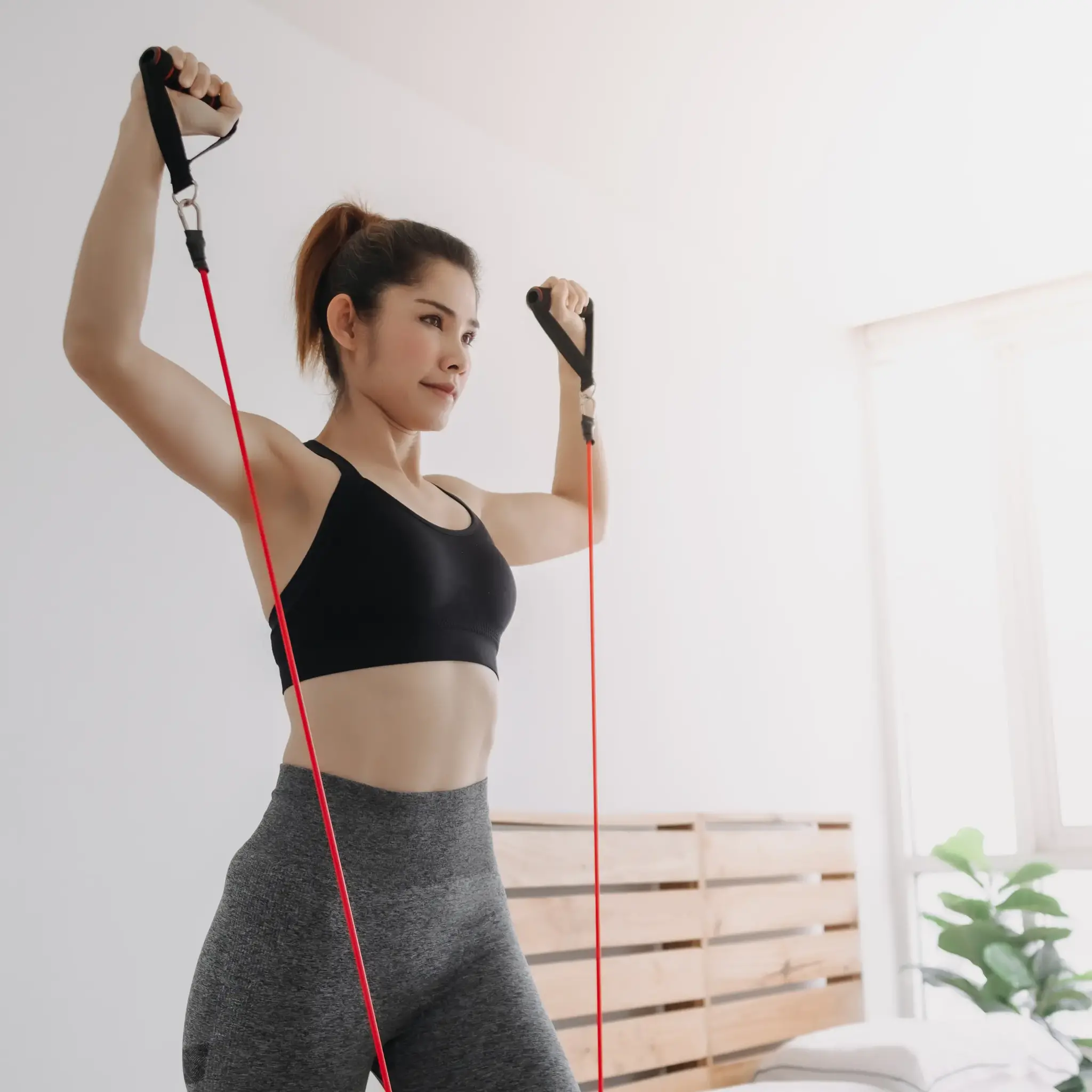 Woman in workout clothes stretching with a red resistance band, indoors with a bright room.
