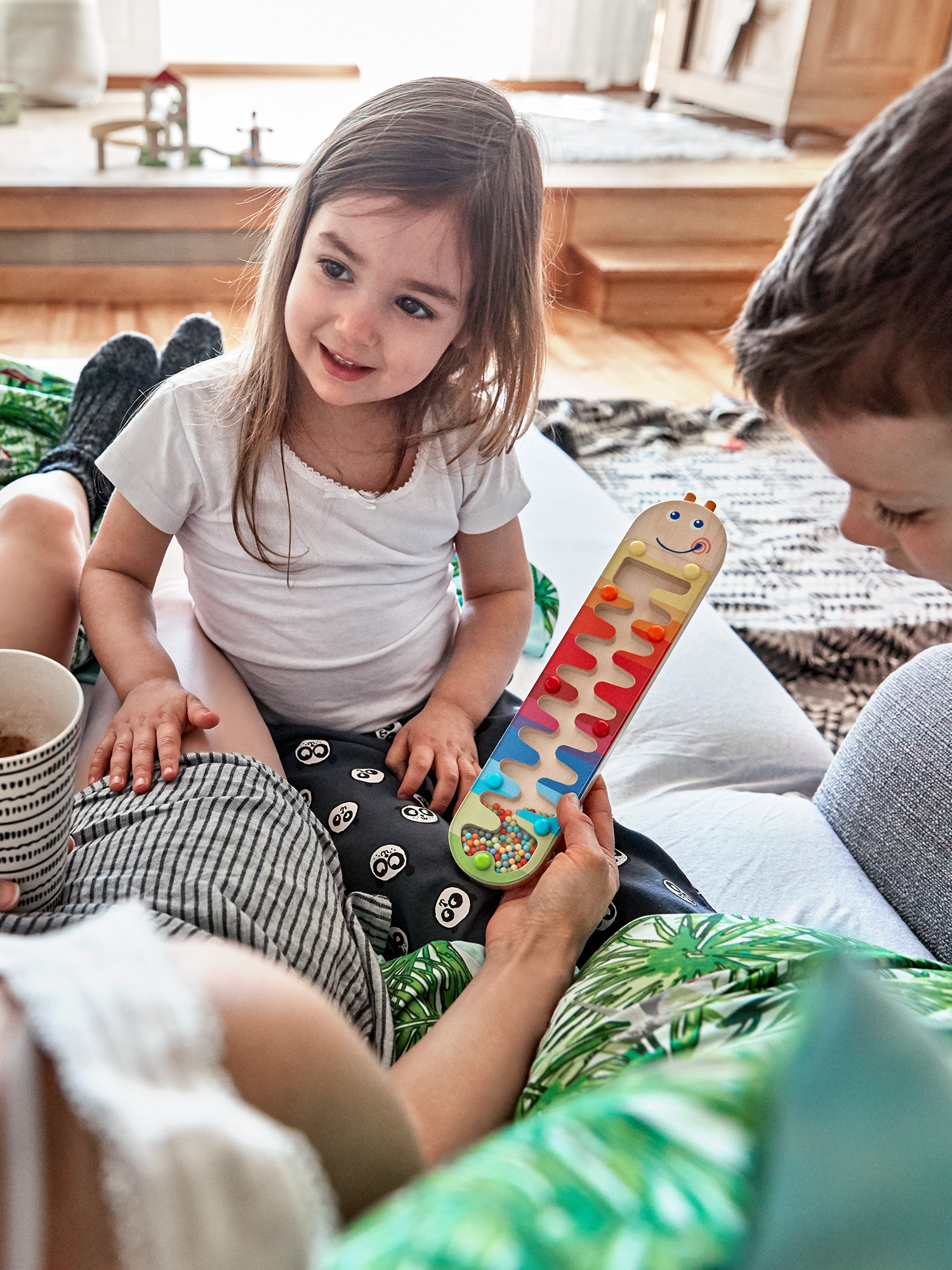 Ein Kind spielt mit einem Spielzeug, während es drinnen mit zwei Erwachsenen auf einer Couch sitzt.