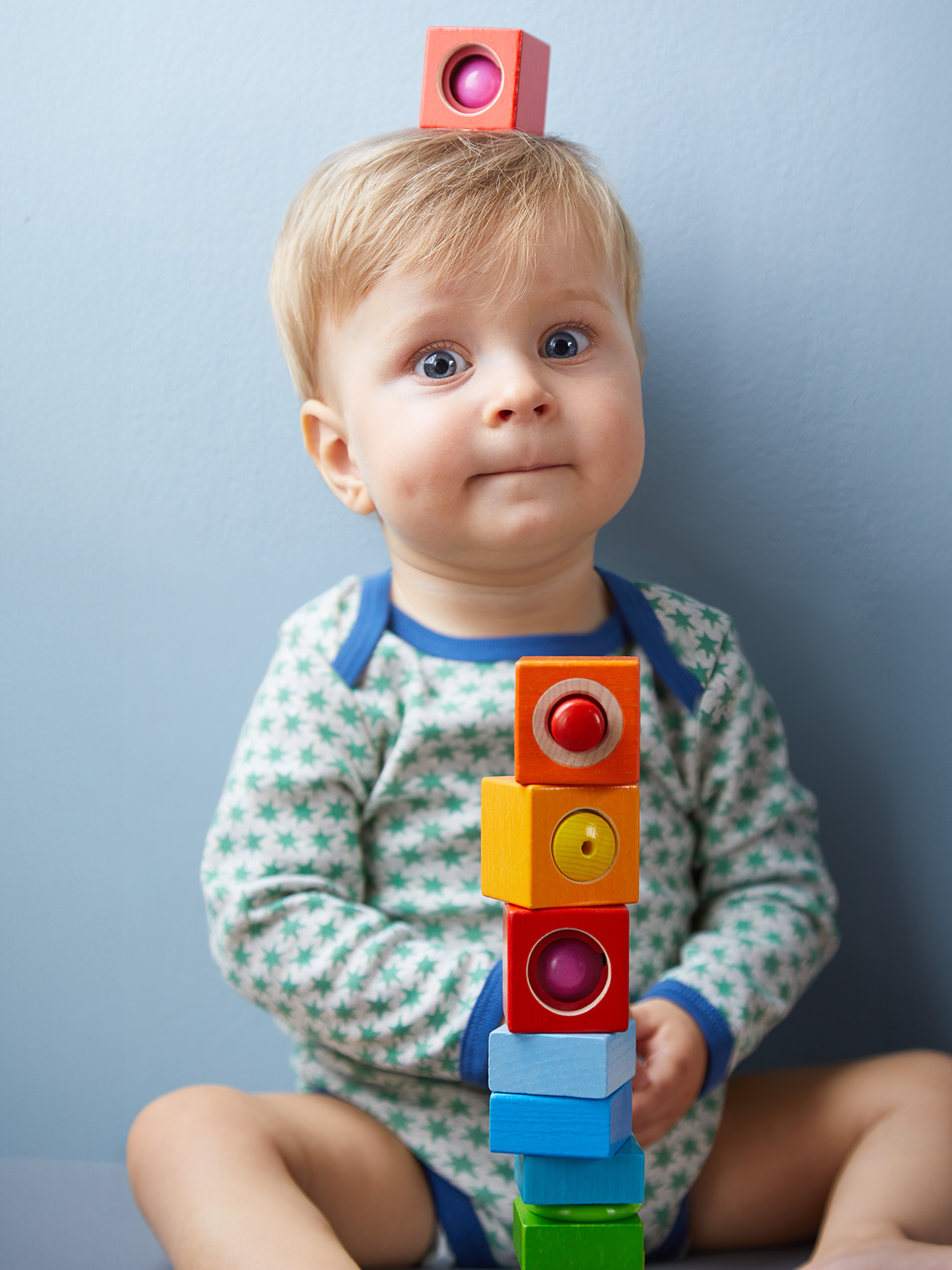 Ein Baby mit einem Stapel bunter Blöcke davor. Die Blöcke sind hoch gestapelt.