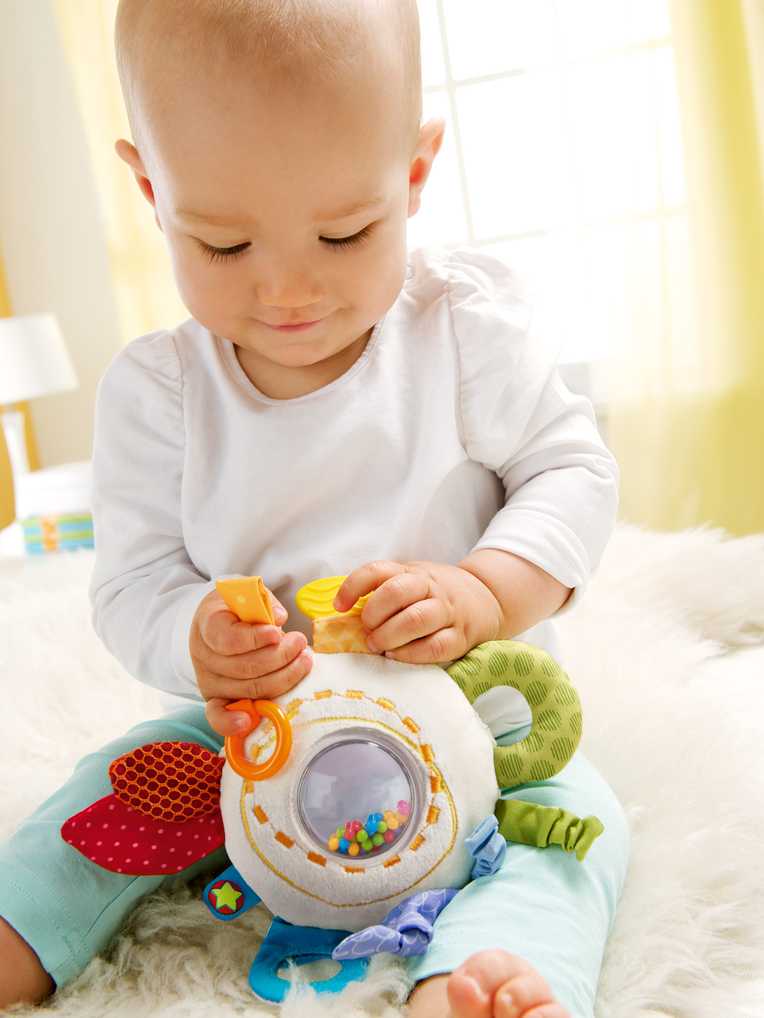 Baby hält ein buntes Spielzeug mit Perlen. Baby trägt ein weißes Hemd und blaue Hose. Weißer Hintergrund.