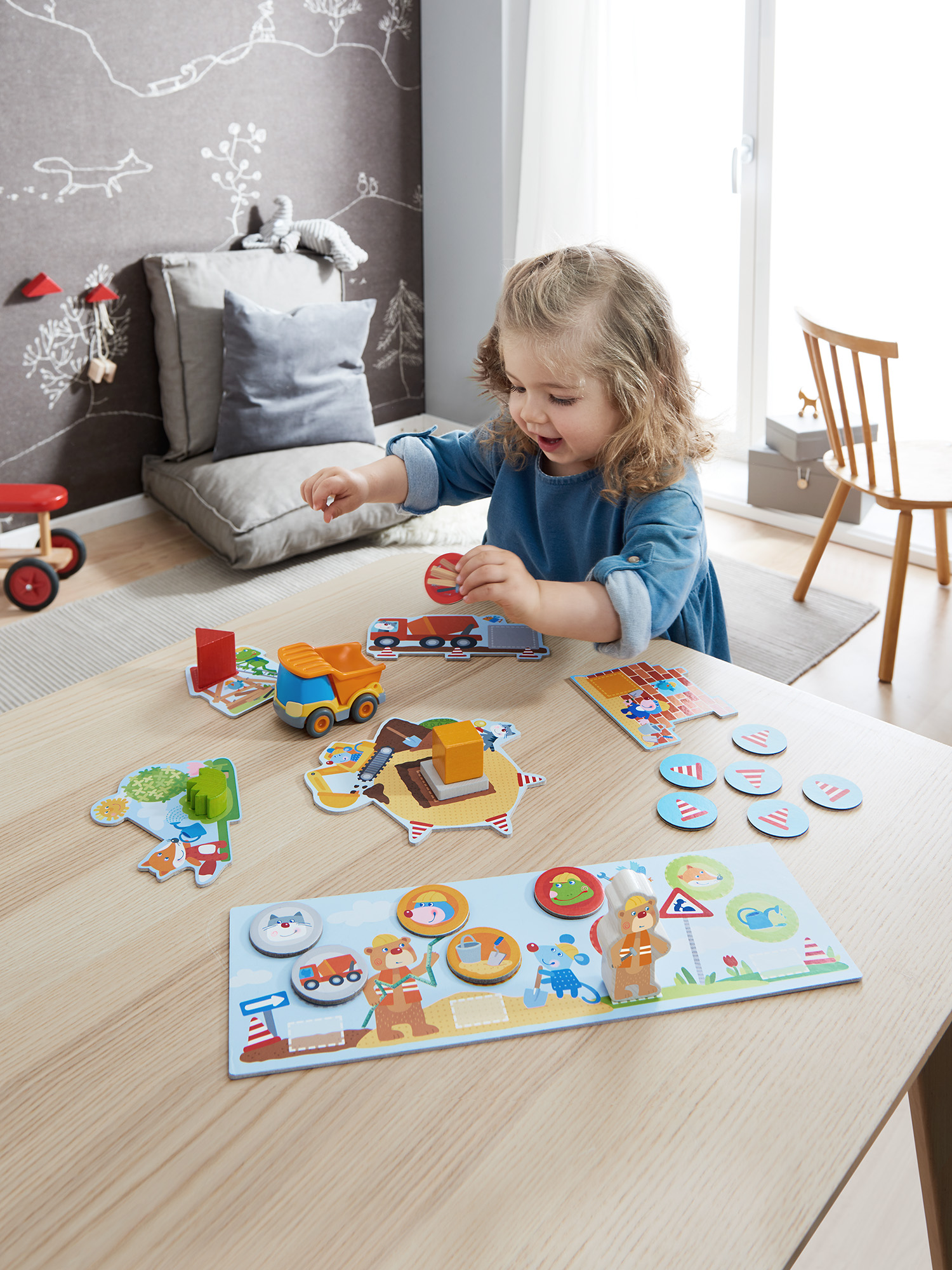 Ein Kind spielt mit Konstruktionsspielzeug auf einem Holztisch. Andere Spielsachen sind herum.