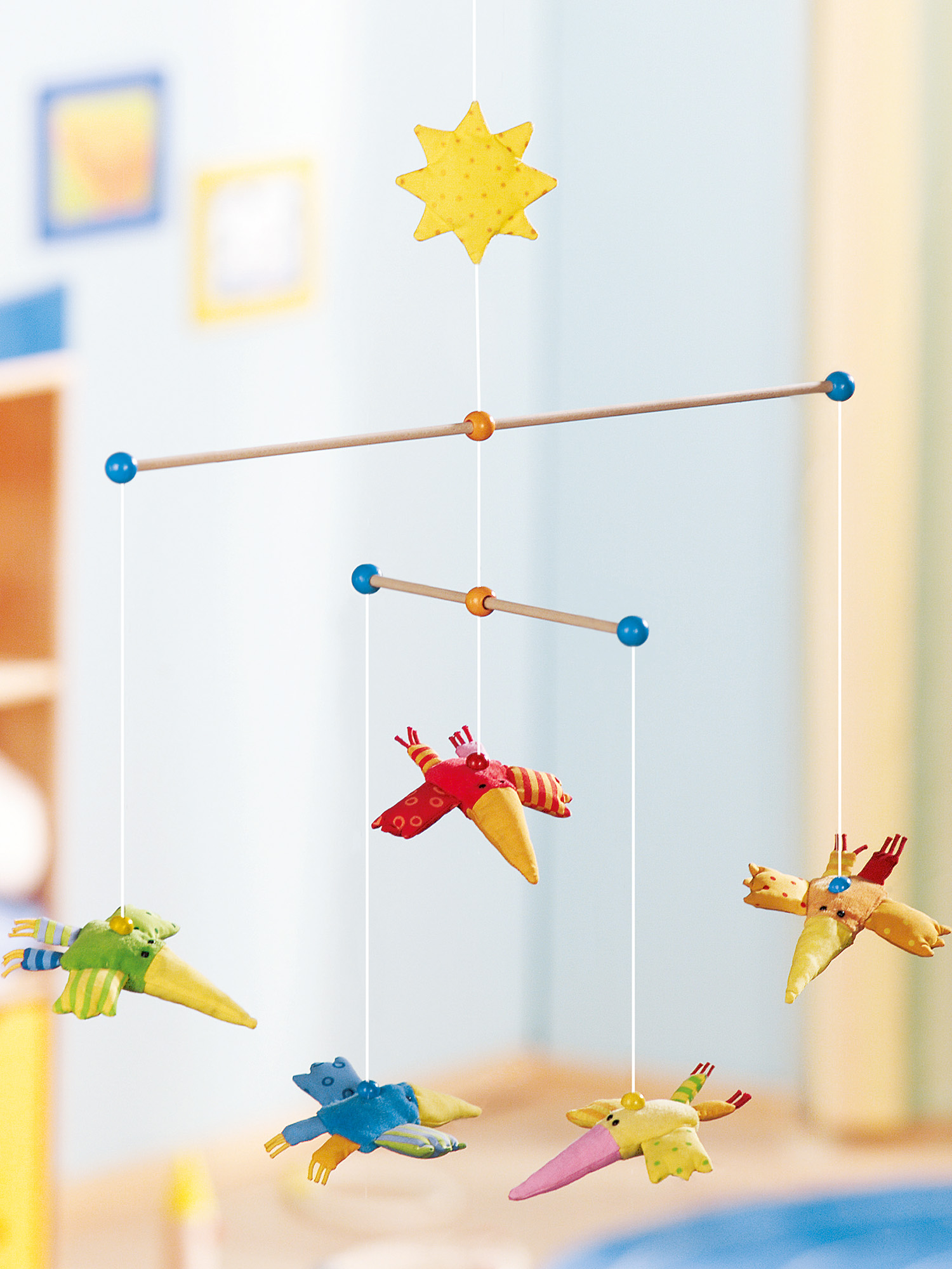 Ein buntes Babymobile mit Stern- und Vogelförmigen Dekorationen. Es hängt an einem Holzrahmen.
