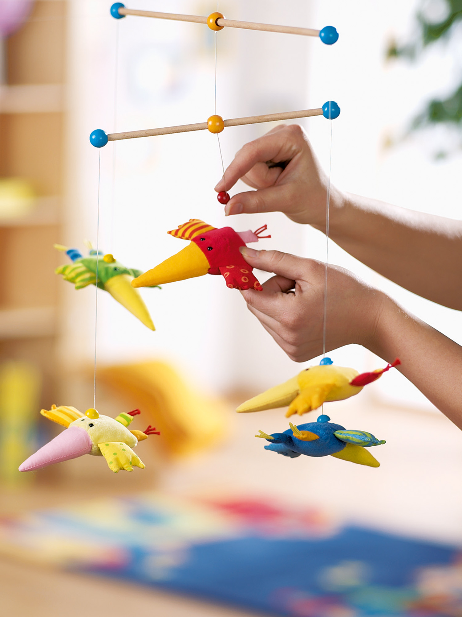 Hände, die ein Babymobile mit Vogelfiguren zusammenbauen. Der Hintergrund hat eine blaue Matte und eine Wand.