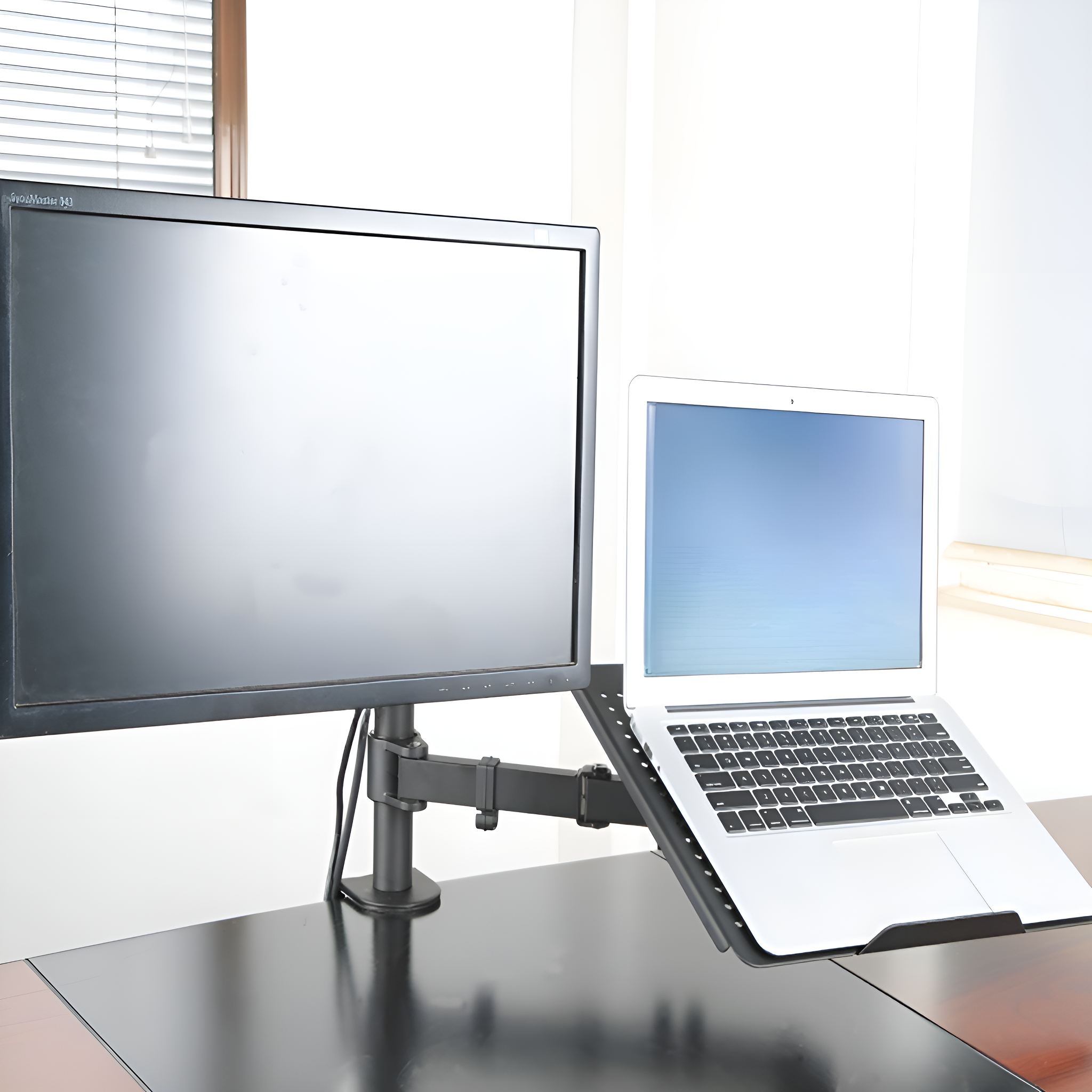Ein Laptop auf einem Ständer neben einem Monitor, beides auf einem schwarzen Schreibtisch.
