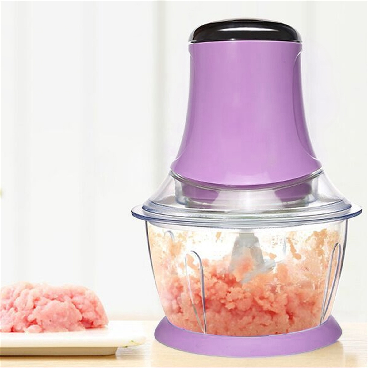 Lila-Lebensmittelzerkleinerer mit einer durchsichtigen Schüssel mit gehacktem rosa Essen. Ein kleiner Haufen Essen.