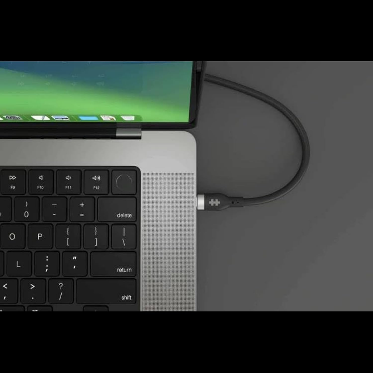 Laptop collegato a un cavo nero, in carica. Il laptop è aperto, mostra uno schermo. Sfondo grigio.