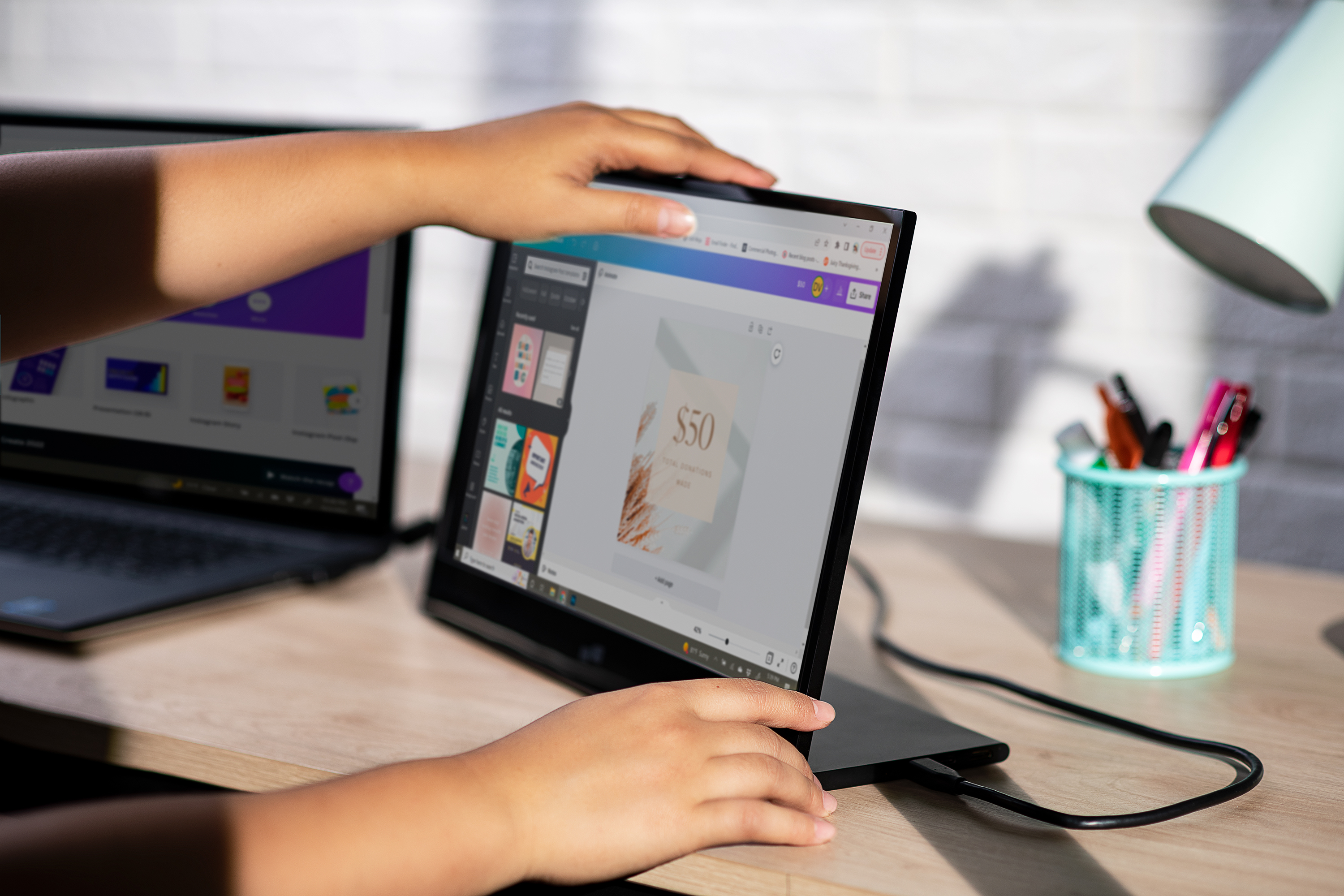 Person verwendet Laptop mit Design auf dem Bildschirm, auf einem Schreibtisch neben Lampe.