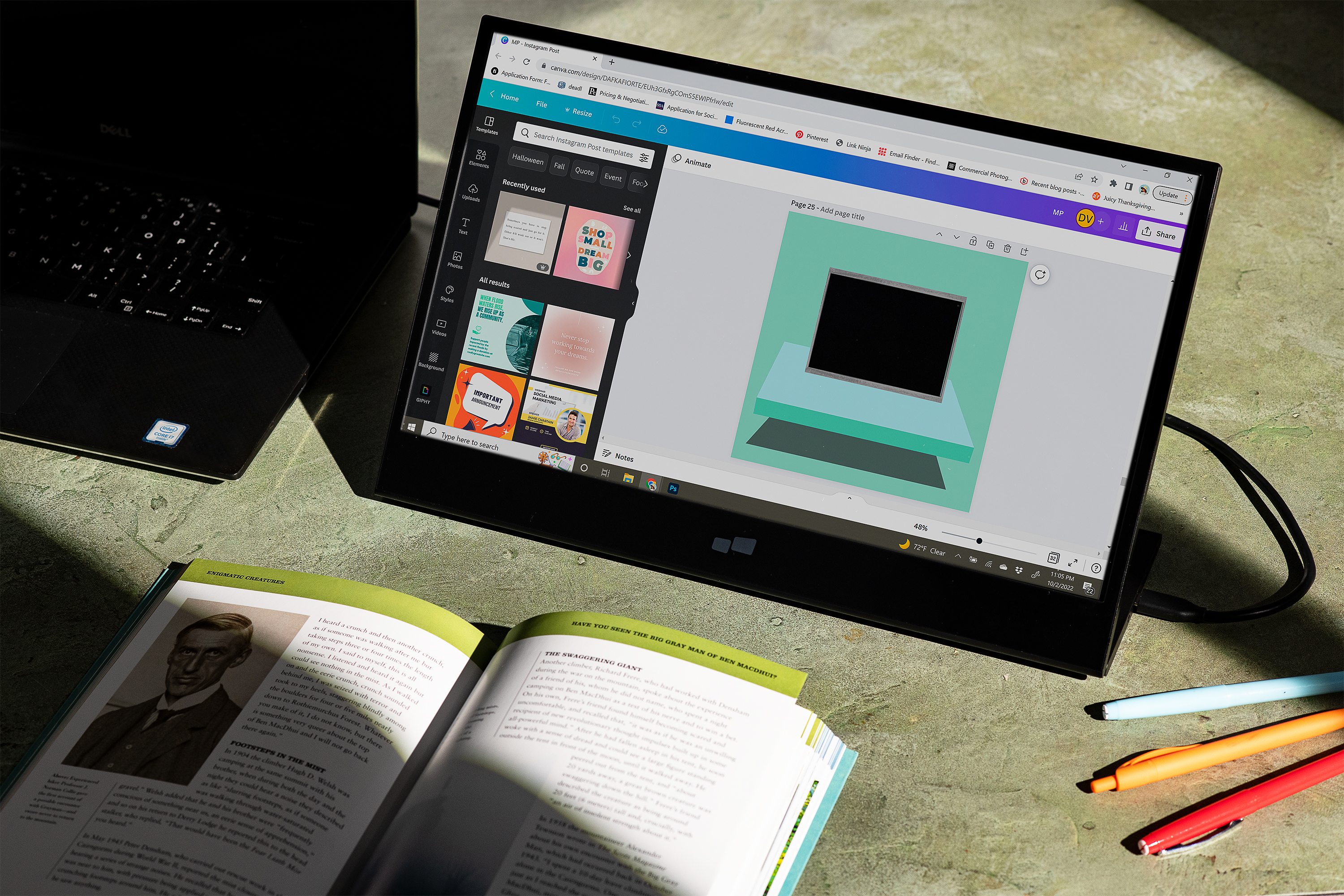 Ein Laptop mit Designoberfläche steht neben einem schwarzen Laptop und einem offenen Buch.