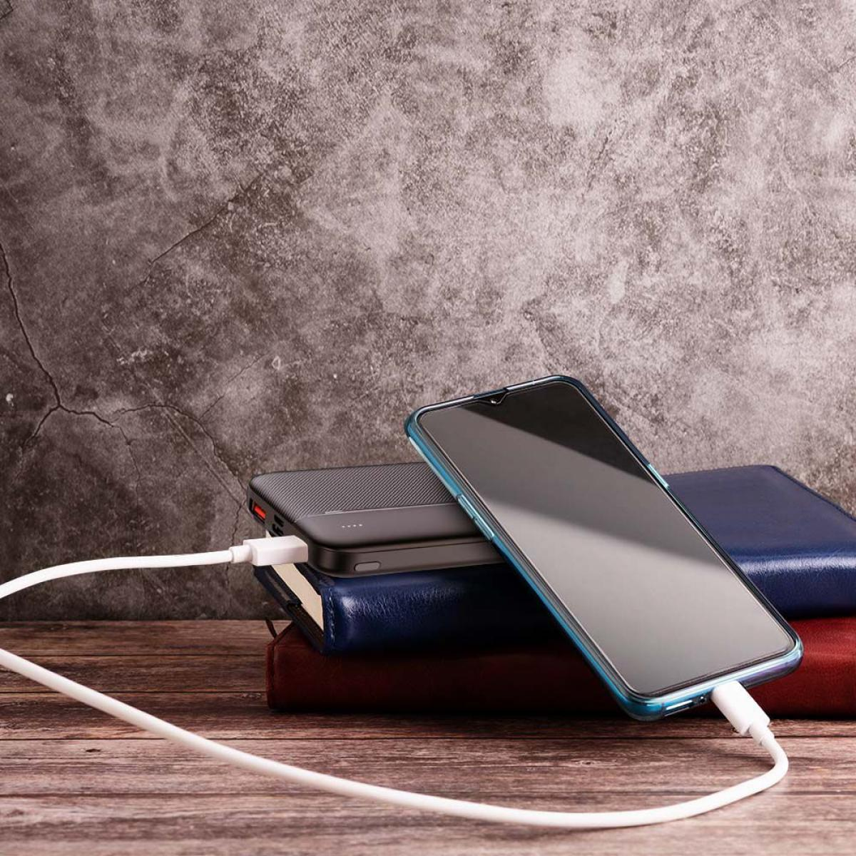 Uno smartphone in carica su un tavolo di legno. È accanto a un power bank e dei libri. Un cavo bianco è collegato.