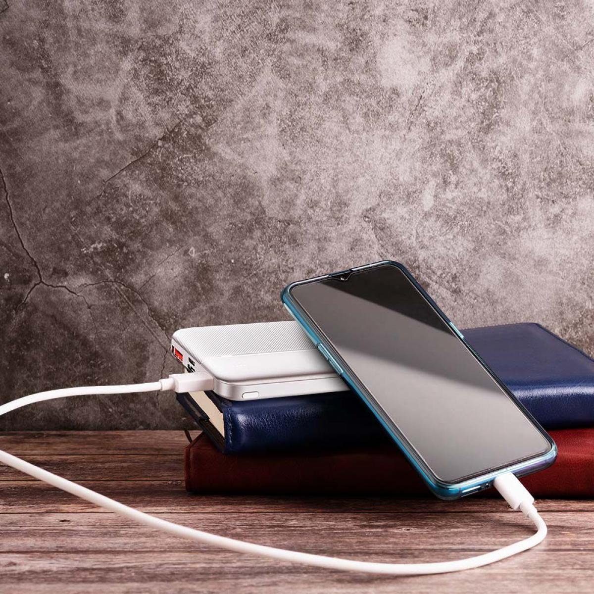 Uno smartphone si carica su un power bank. Libri sullo sfondo. Un cavo bianco li collega.
