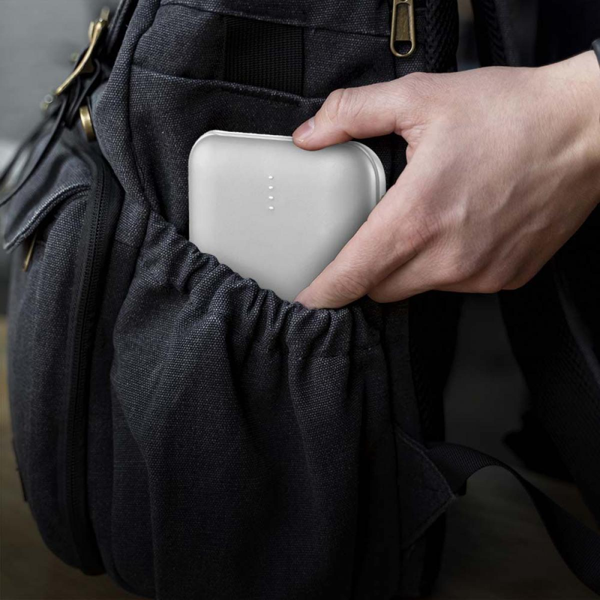 Una mano che raggiunge la tasca di uno zaino nero, estraendo un power bank bianco.