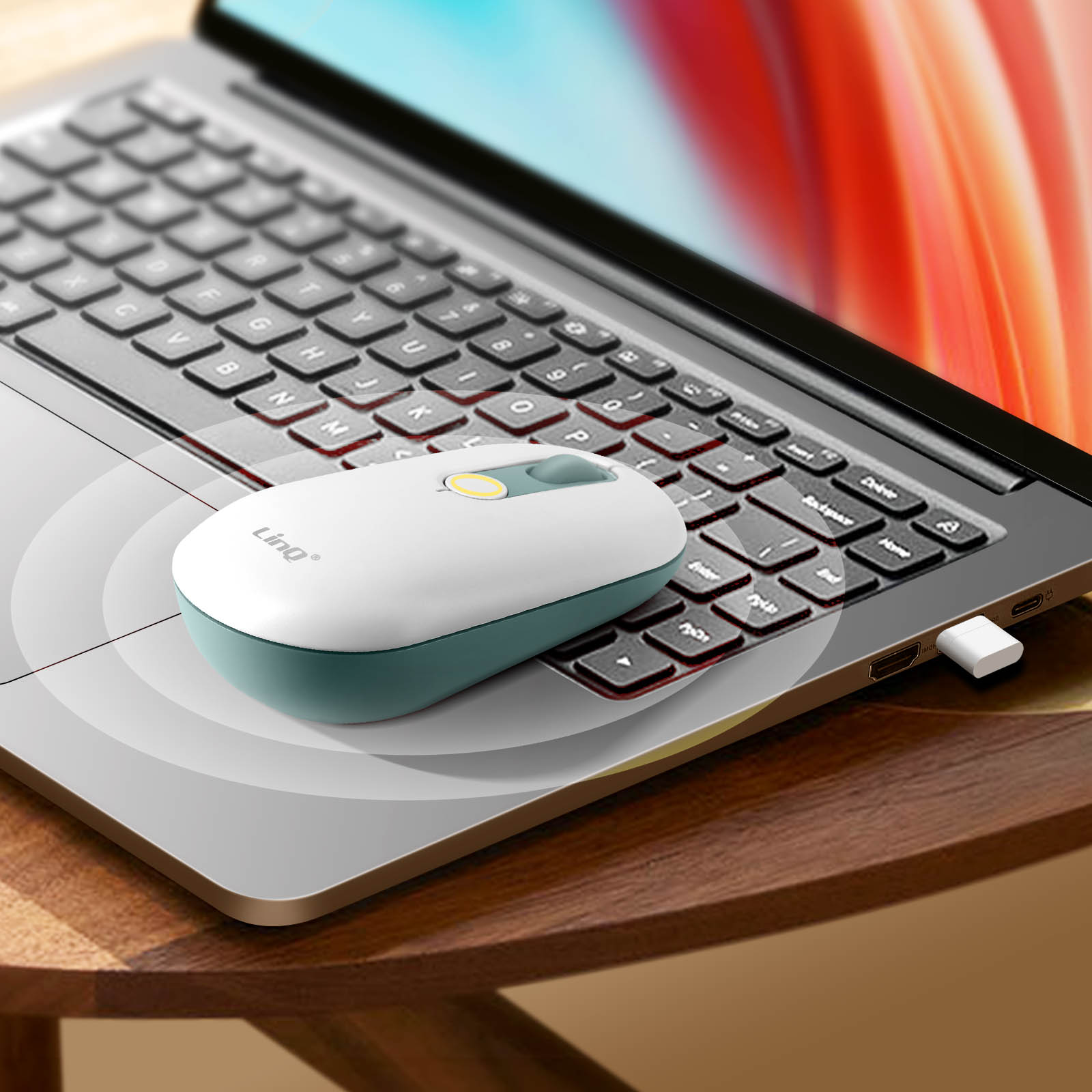 Mouse wireless bianco e verde acqua su un laptop. Il laptop è su un tavolo di legno.