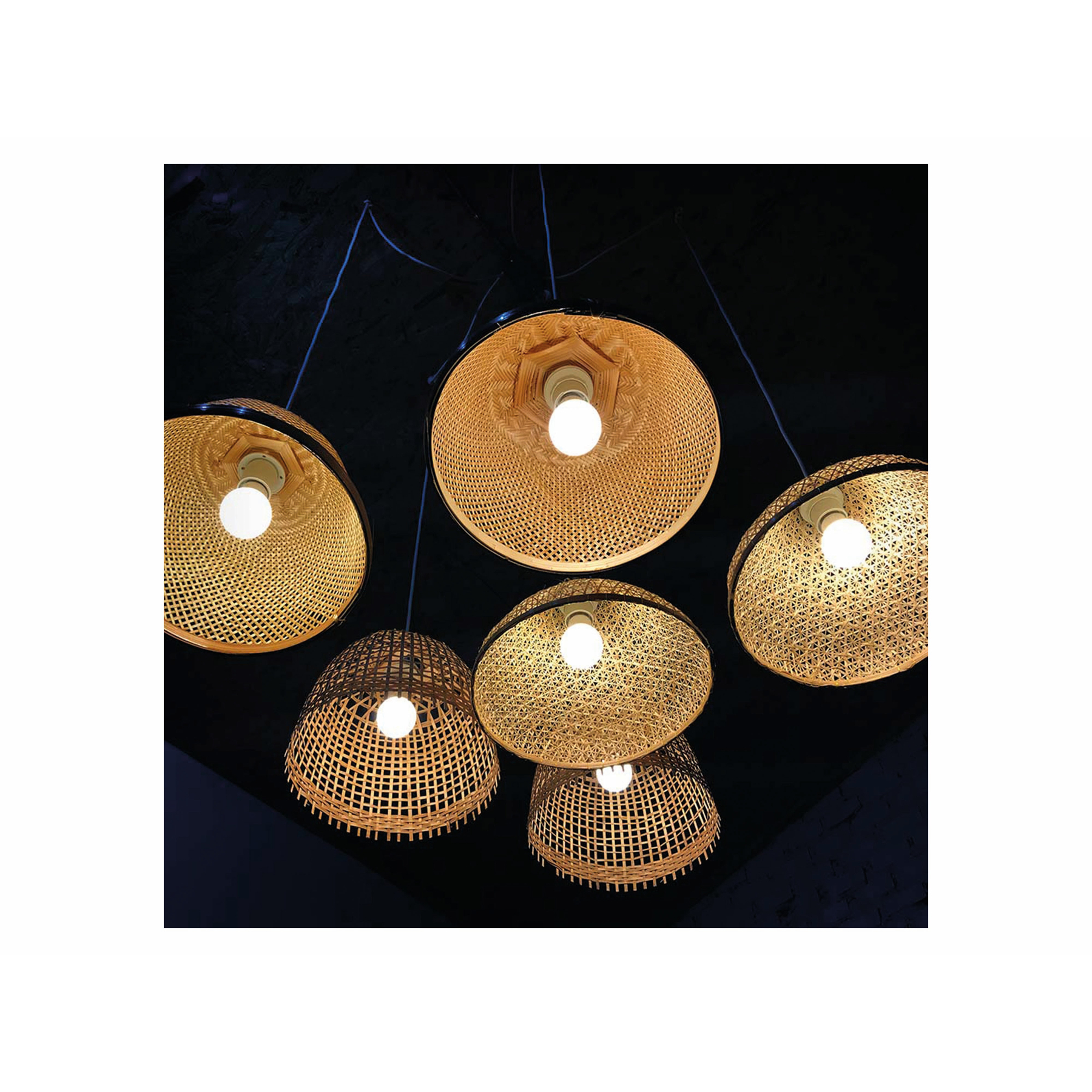 Diverse lampade in rattan appese a un soffitto scuro con luci accese, che illuminano l'area sottostante.