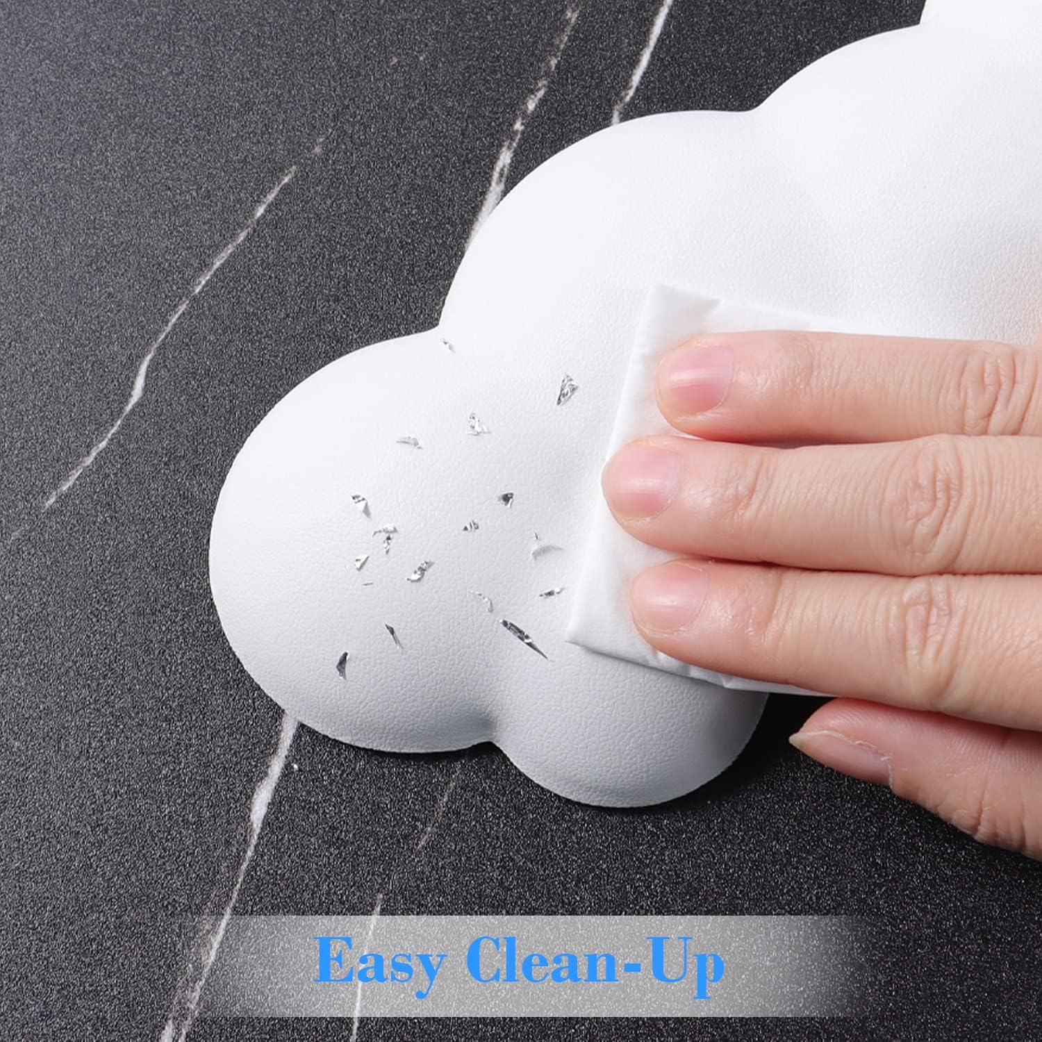 Un objet blanc en forme de nuage est nettoyé avec une lingette sur une surface sombre marbrée.