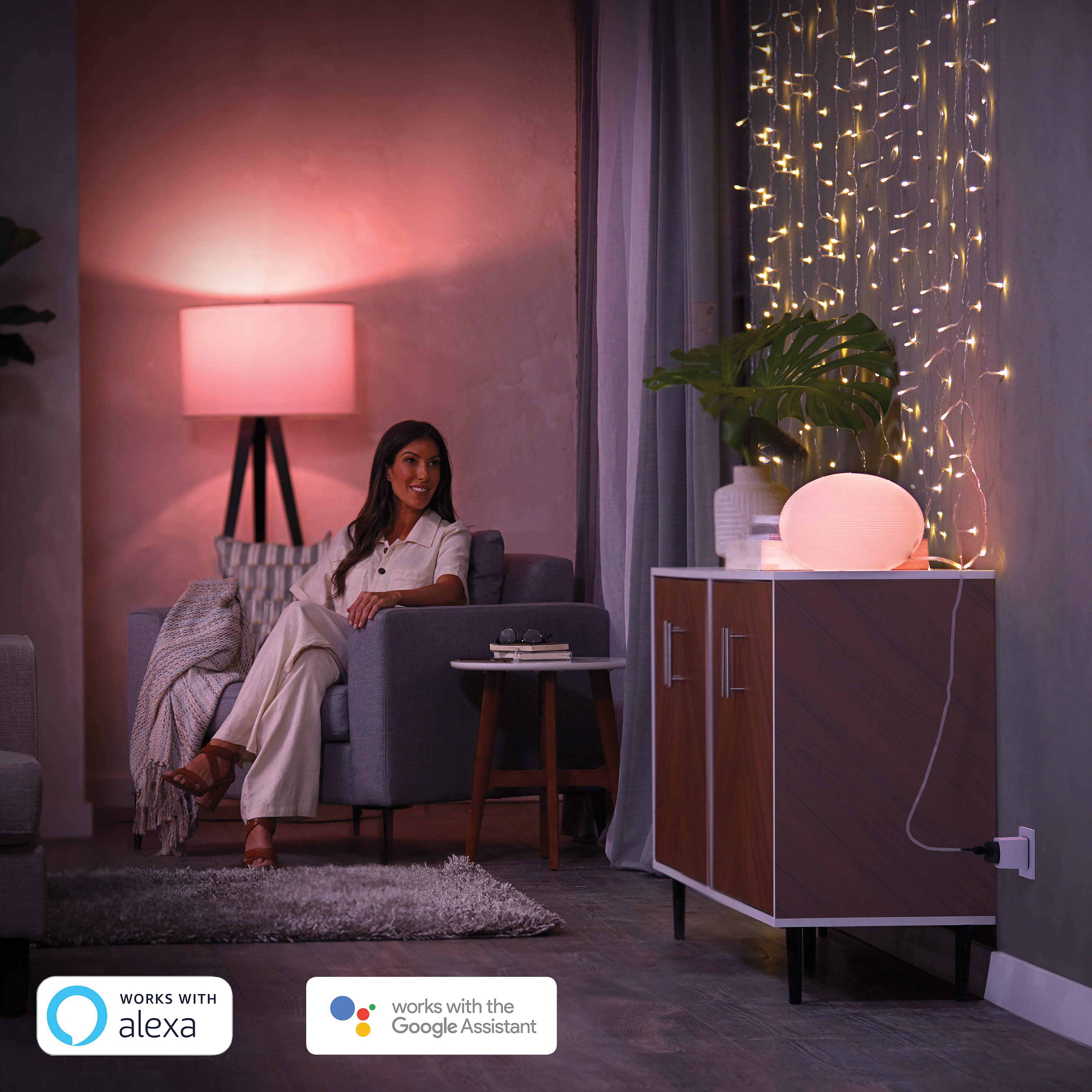 Una donna seduta, che guarda una lampada. Un mobile e luci a catena sono sullo sfondo.