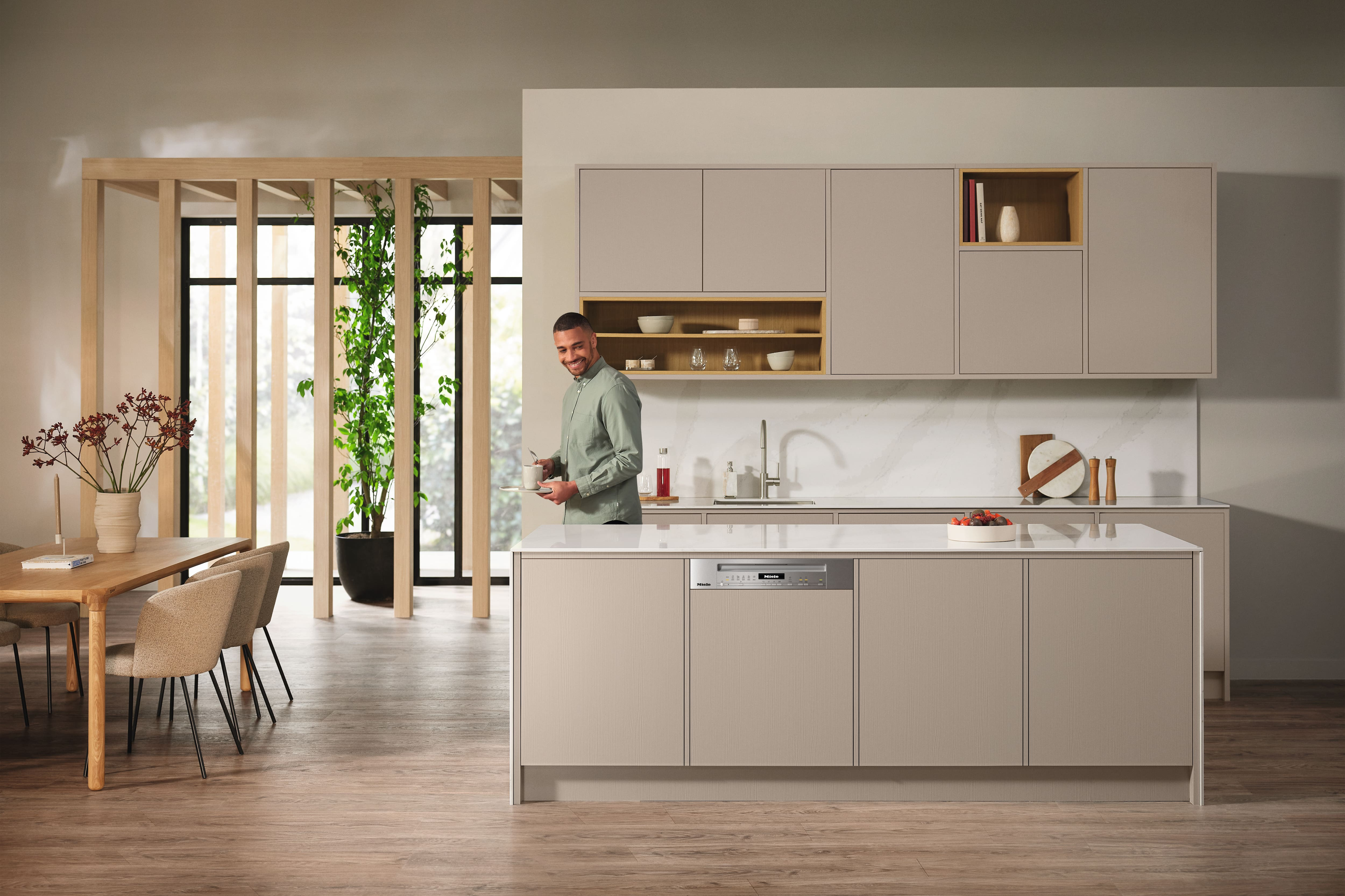 Moderne Küche mit Mann. Beige Schränke, Insel und Holzakzente.