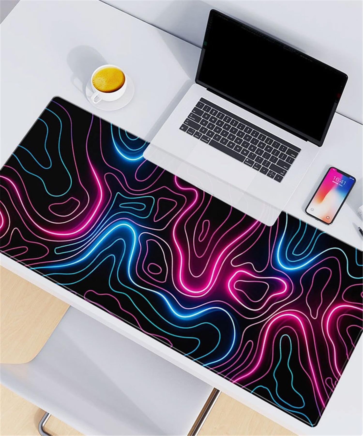 Biurko z kolorową podkładką pod mysz z neonowym wzorem, laptopem, telefonem i filiżanką kawy.