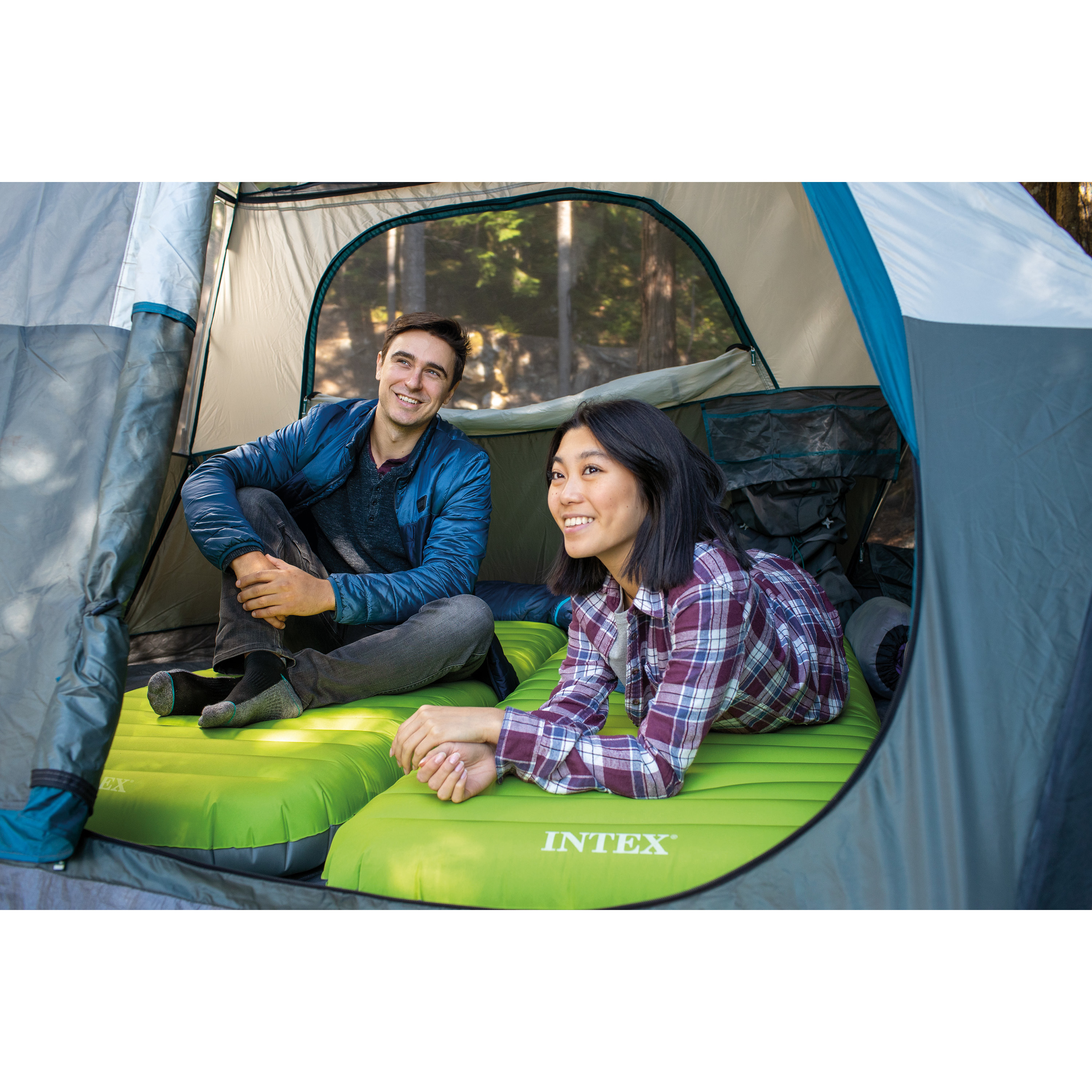 Twee mensen ontspannen op een groen opblaasbaar matras in een tent. Ze glimlachen.