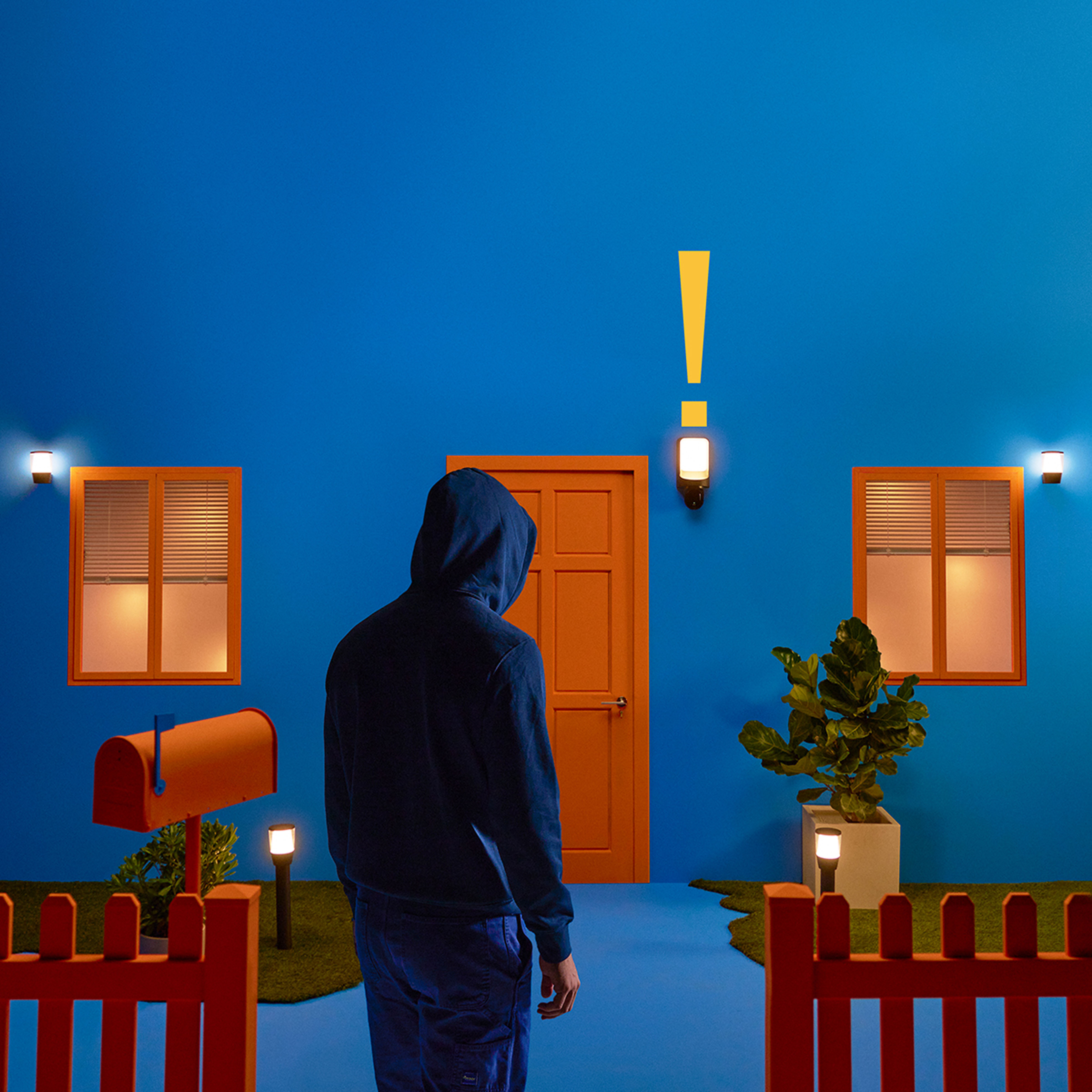 Person in front of a blue house, with a mailbox and a red fence.