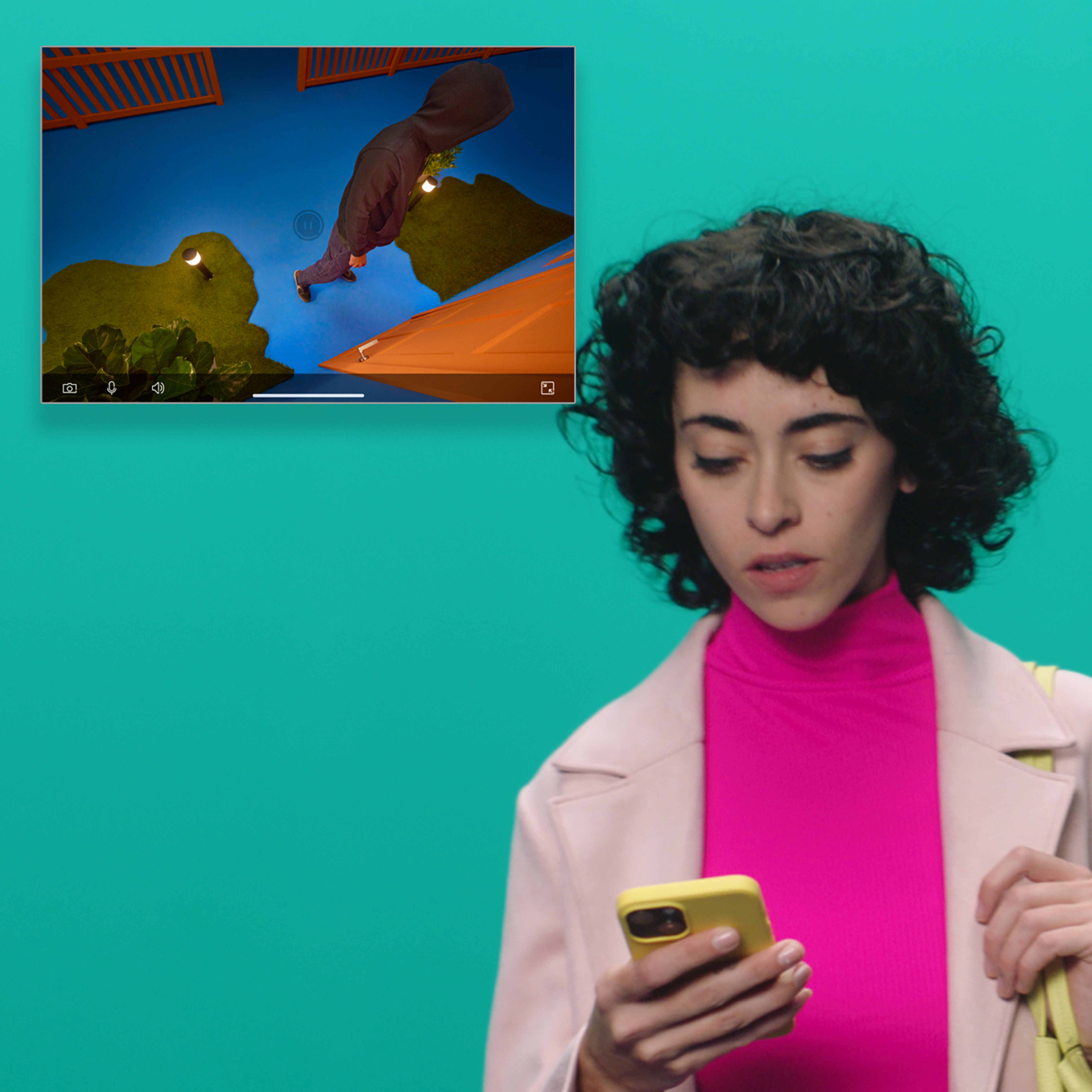 A woman looking at her phone, with a video playing on the screen behind her.
