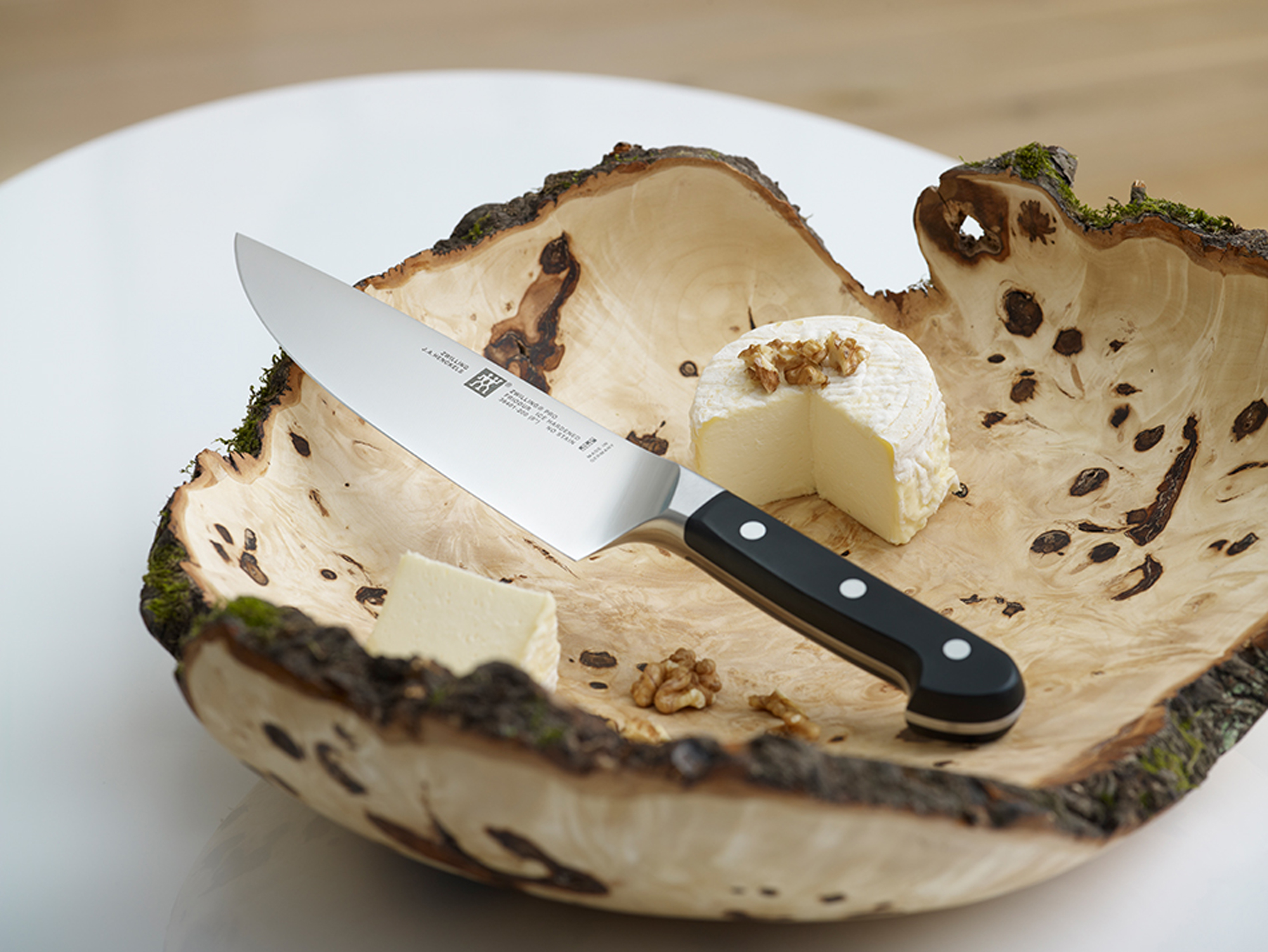 Nóż na drewnianej misce z serem i orzechami włoskimi. Scena jest dobrze oświetlona i artystyczna.
