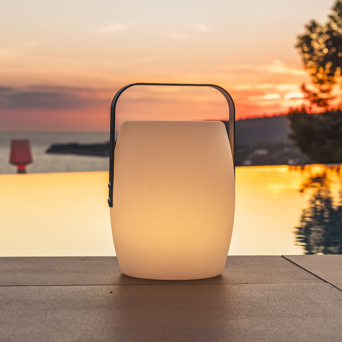 Beleuchtete Außenlampe mit Griff, am Pool bei Sonnenuntergang.