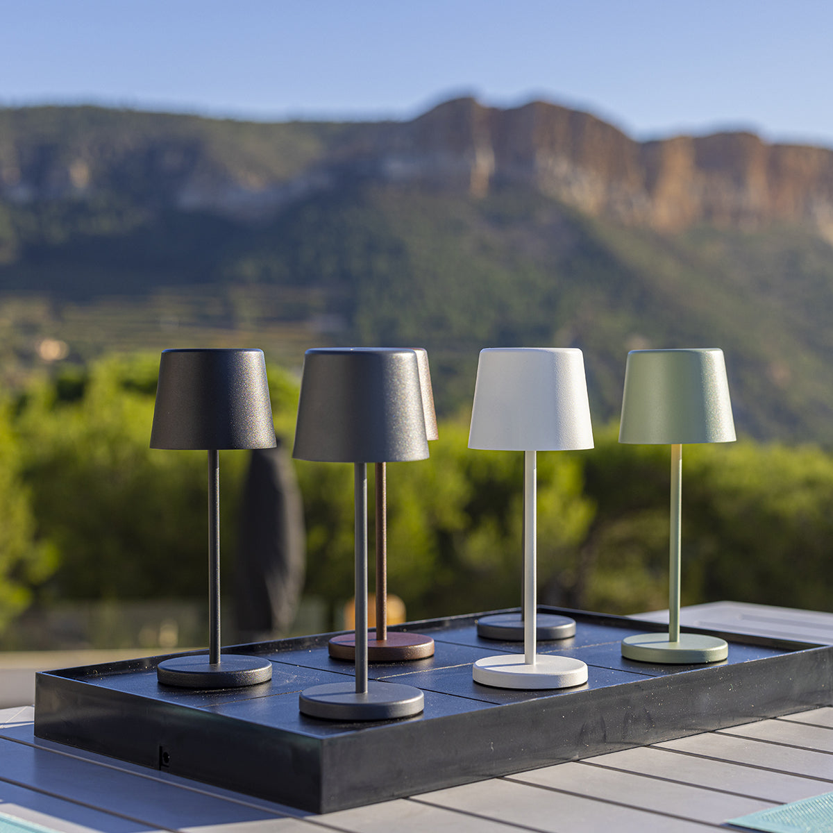 Vier moderne schwarz-weiße Lampen auf einem Tablett. Berge im Hintergrund.
