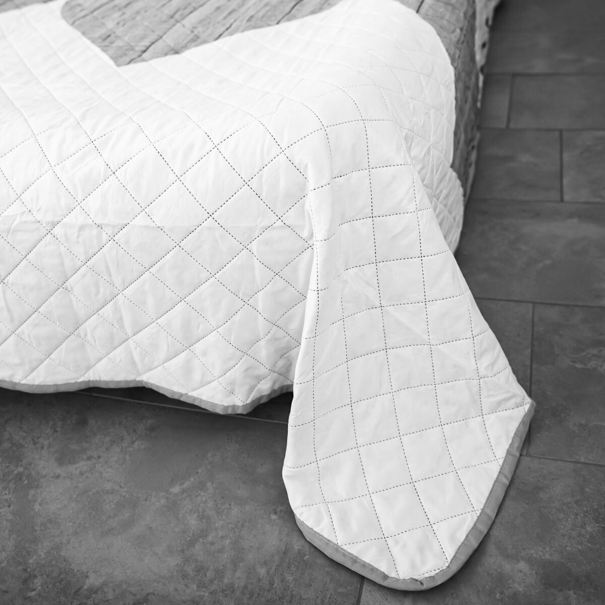 Ein weißes Bett mit einer weiß gemusterten Steppdecke.